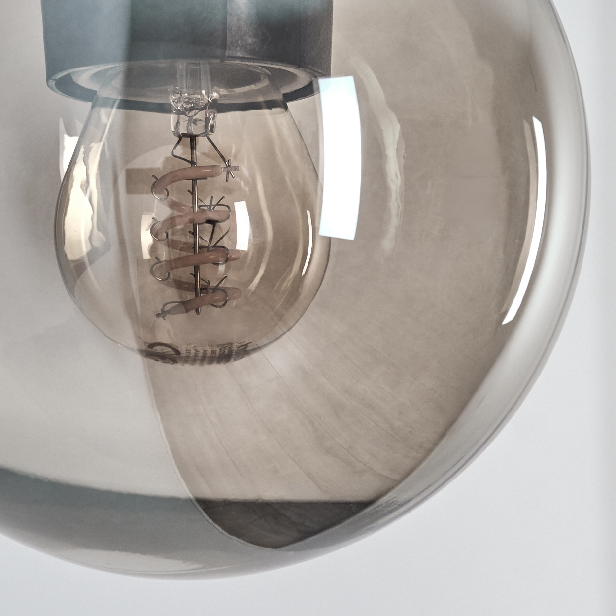 Nahaufnahme einer Glühbirne mit Spiralfilament in einem rauchgrauen Glaslampenschirm.