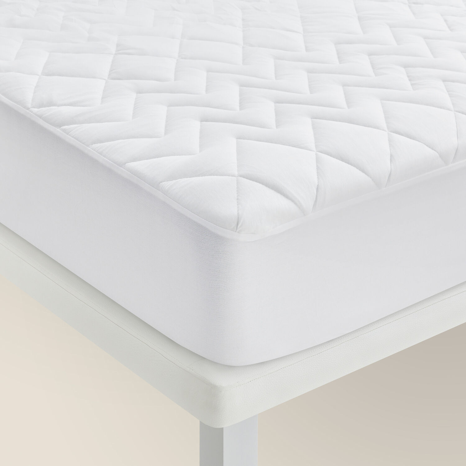 Protector de colchón blanco acolchado sobre un marco de cama blanco.