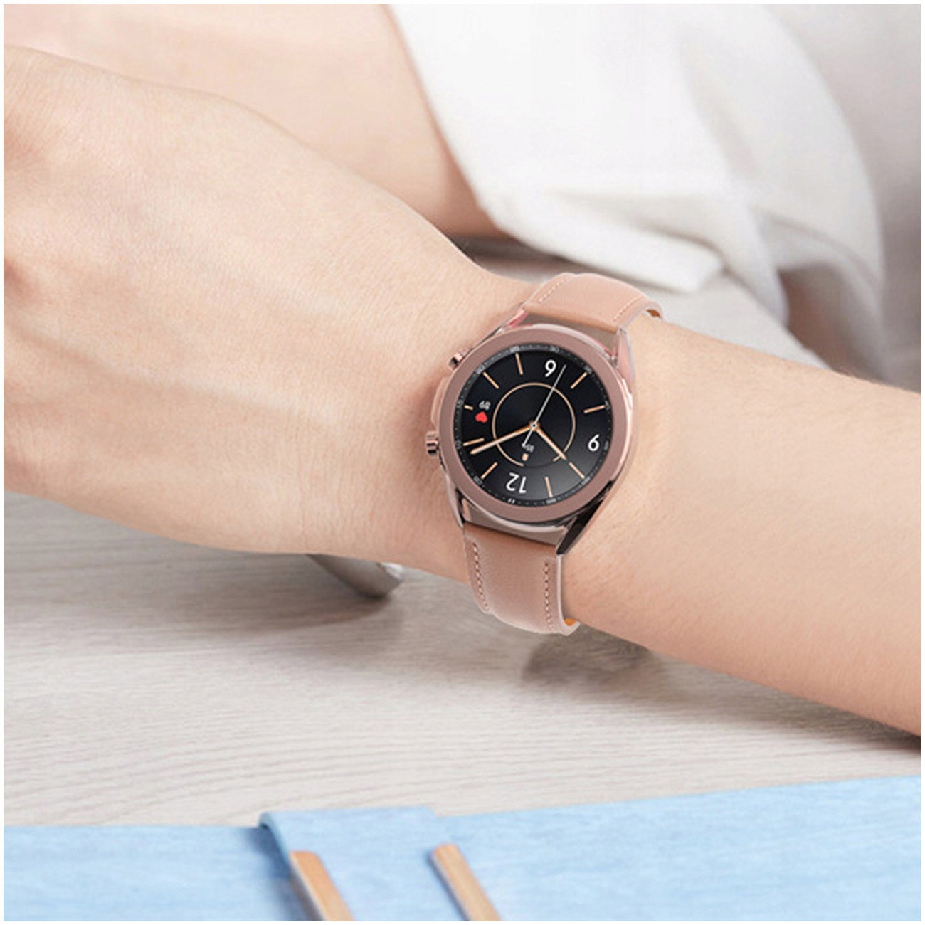Osoba nosi na lewym nadgarstku różowo-złoty smartwatch z brązowym skórzanym paskiem.