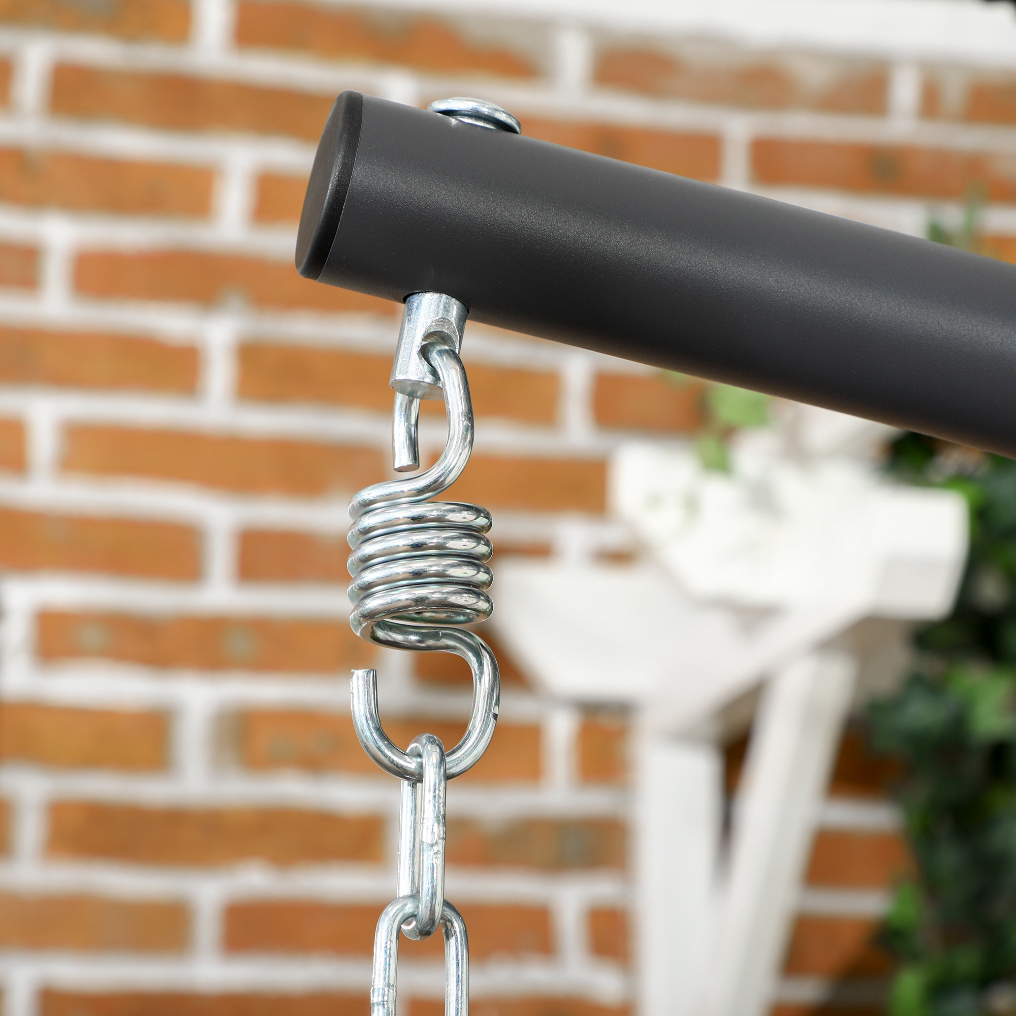 Un resorte y cadena de metal cuelgan de una barra de metal oscura contra una pared de ladrillos.