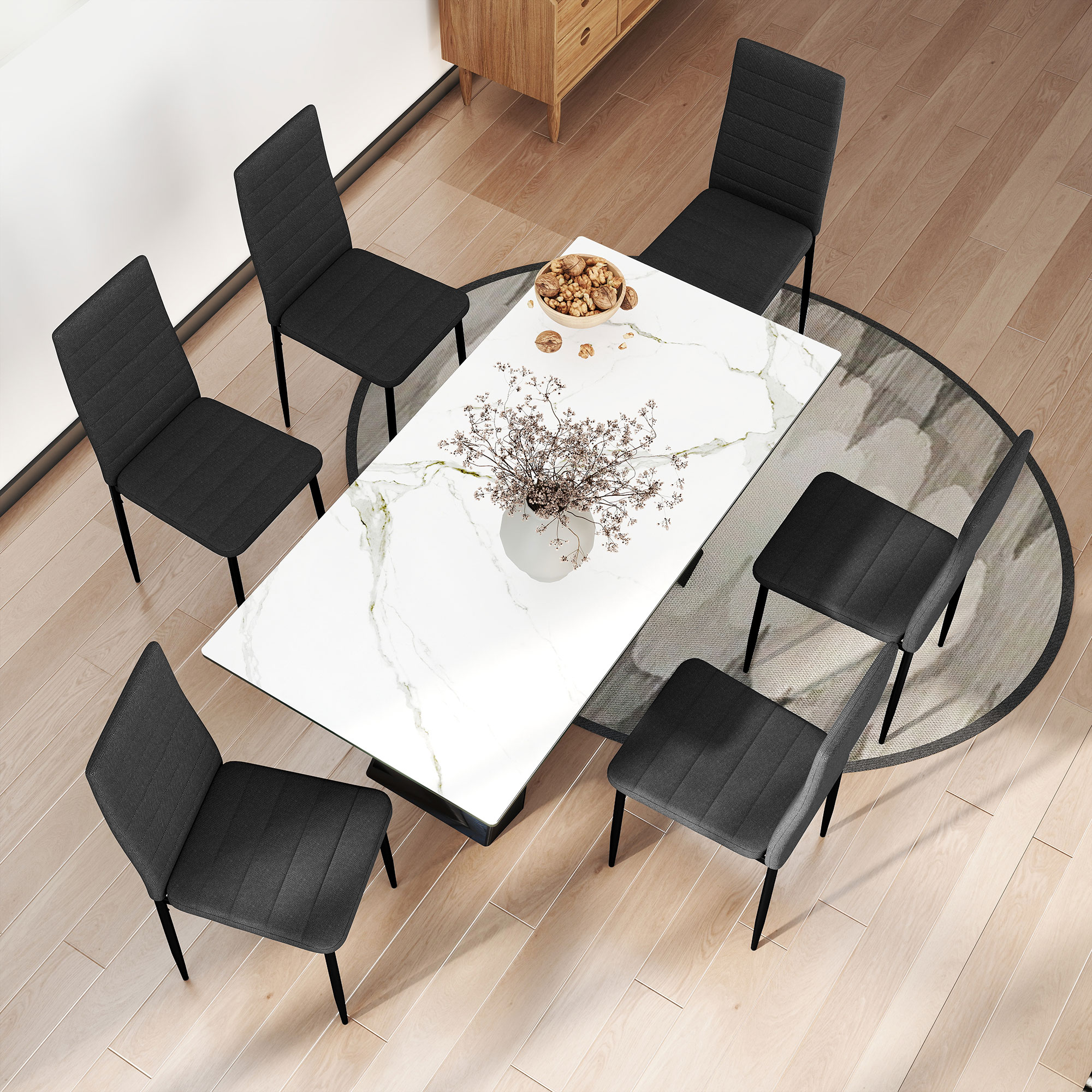 Una mesa de comedor con tapa de mármol blanco rodeada de seis sillas oscuras sobre una alfombra redonda.