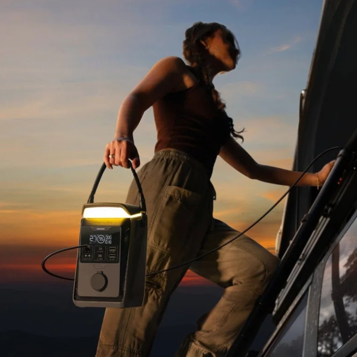 Donna con centrale elettrica portatile sale sul camper al tramonto.