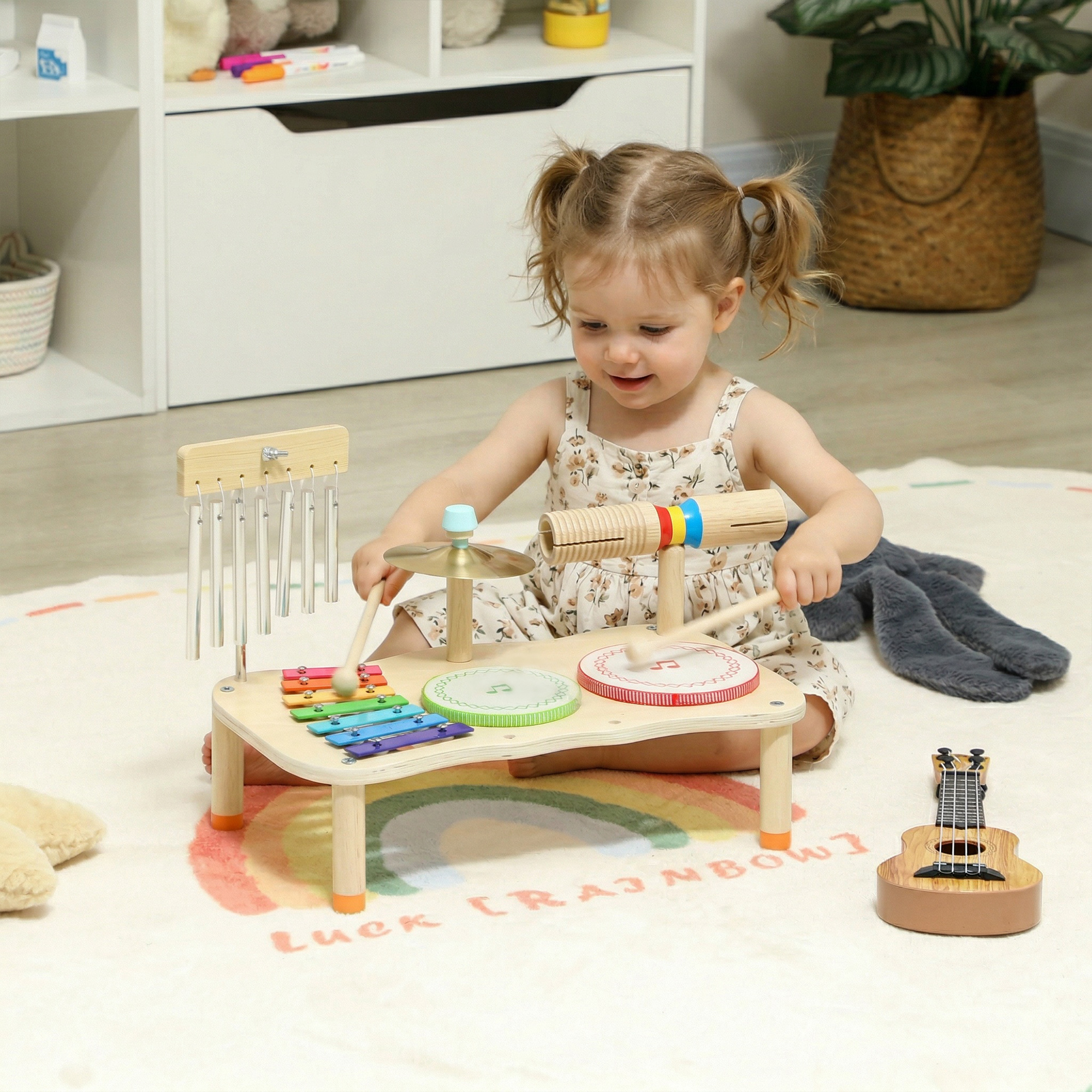 Una niña pequeña toca un set de instrumentos musicales de madera sobre una alfombra de arcoíris. Una ukelele de juguete está cerca.
