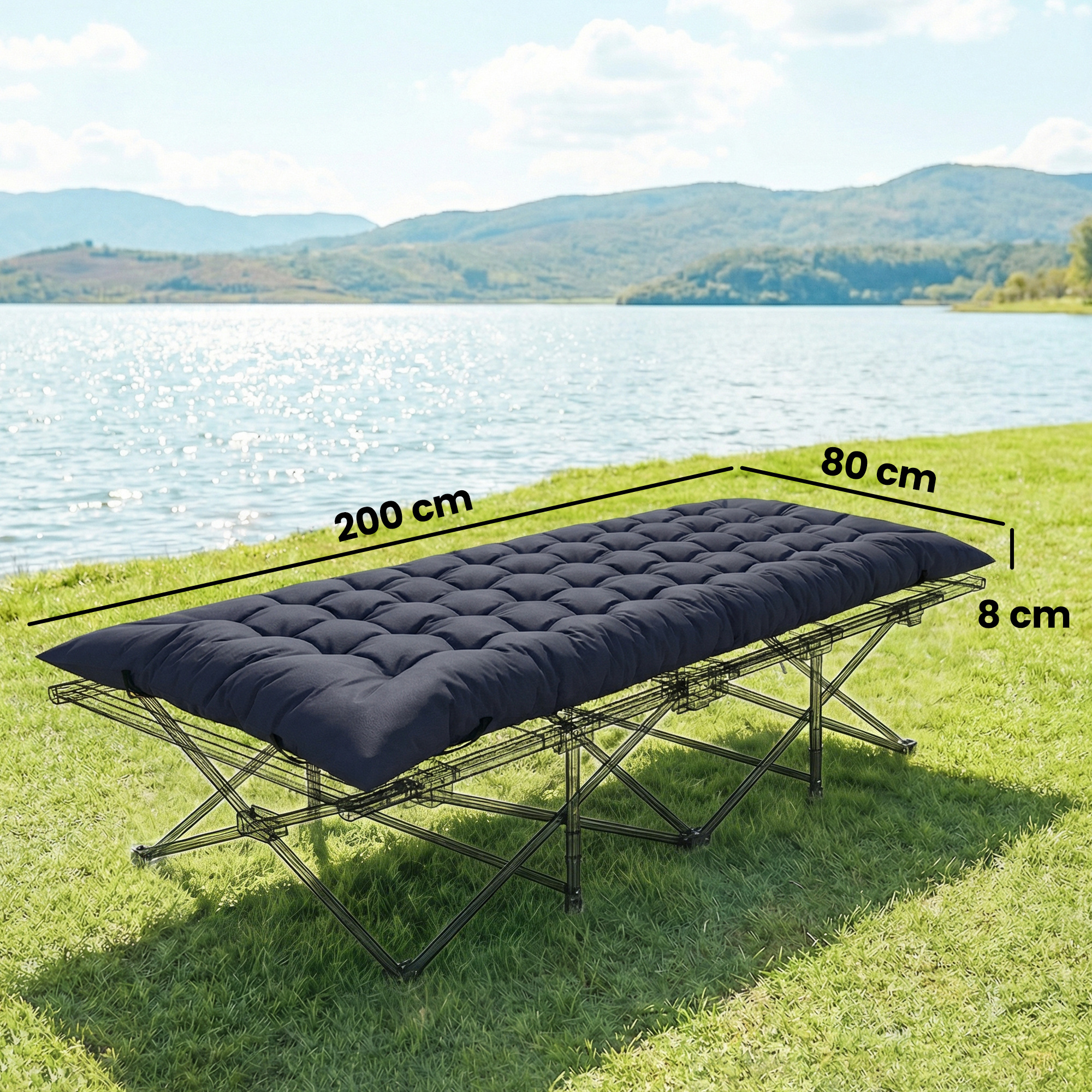 Cama plegable azul oscuro con colchón sobre césped junto a un lago brillante.