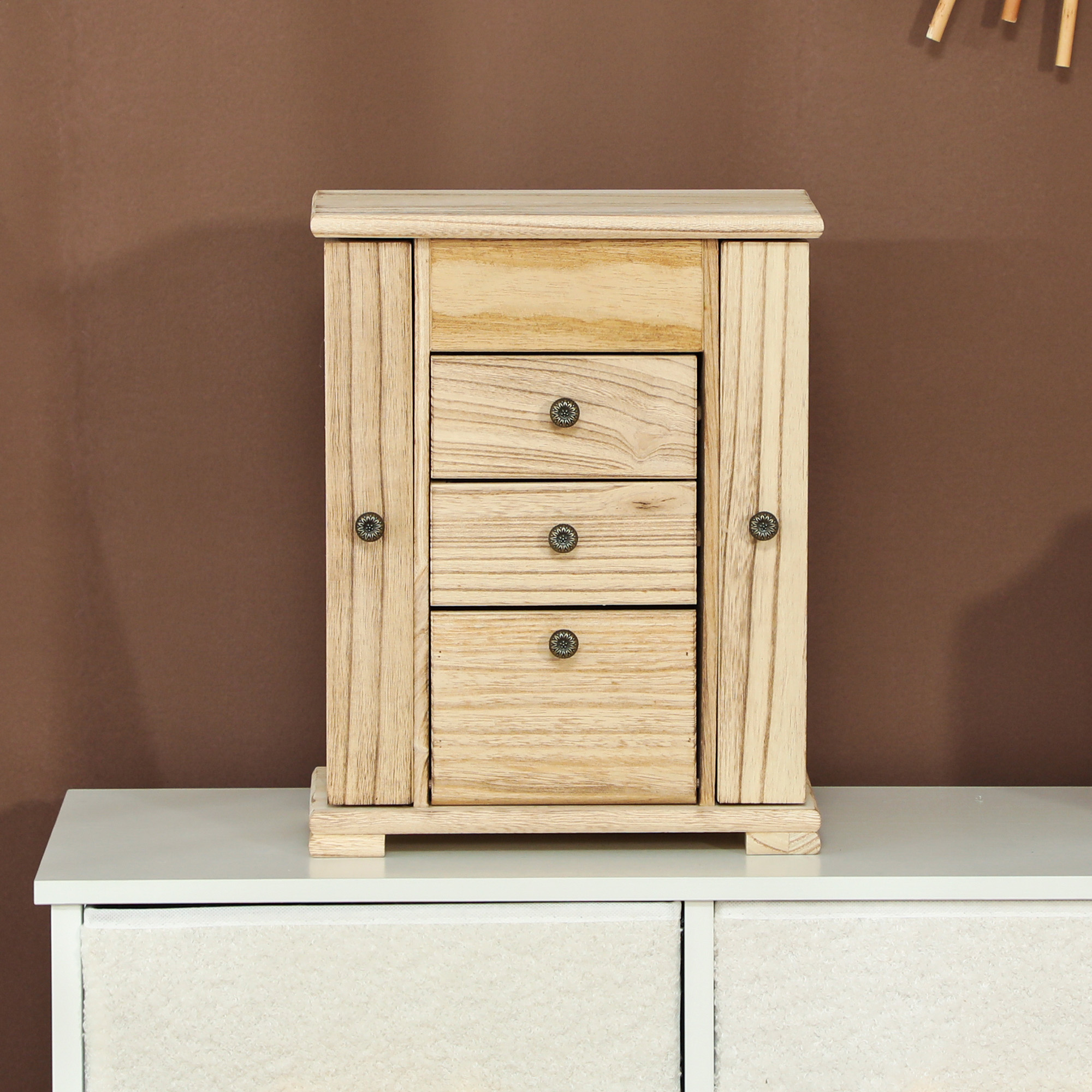 Joyero de madera con tres cajones sobre una mesa blanca.