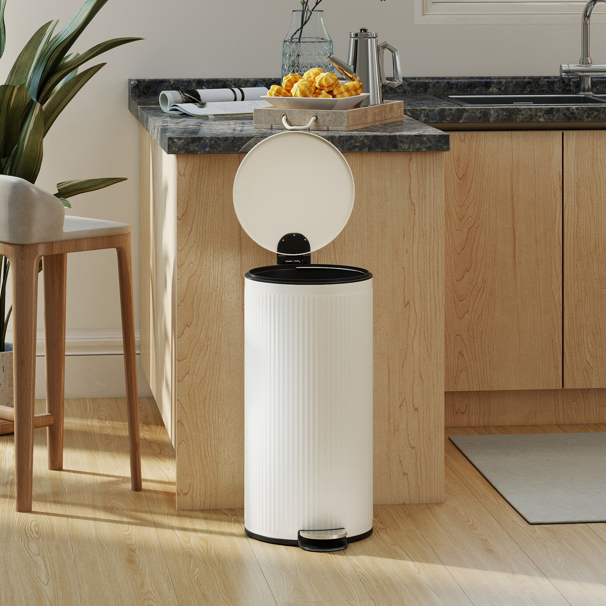 Un cubo de basura blanco con pedal se encuentra sobre suelo de madera junto a armarios de cocina.