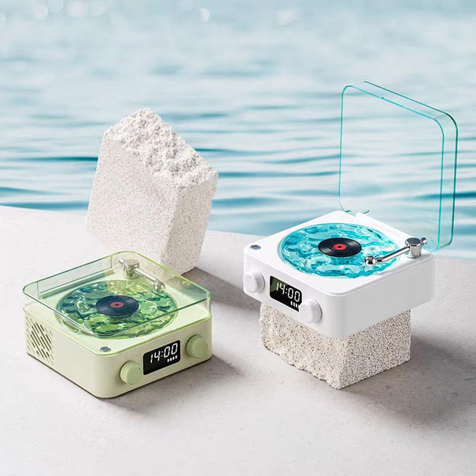 Zwei Retro-Plattenspieler, einer hellgrün, einer weiß, stehen auf Steinblöcken vor blauem Wasser.