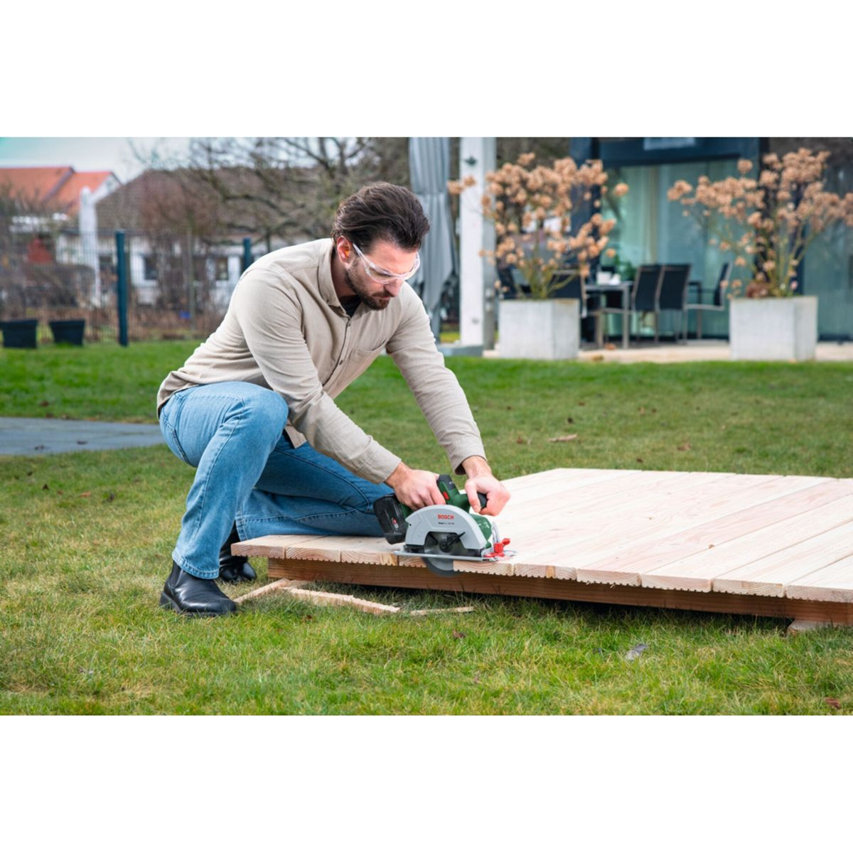 Mann mit Schutzbrille schneidet mit Kreissäge Holzplanken im Freien.