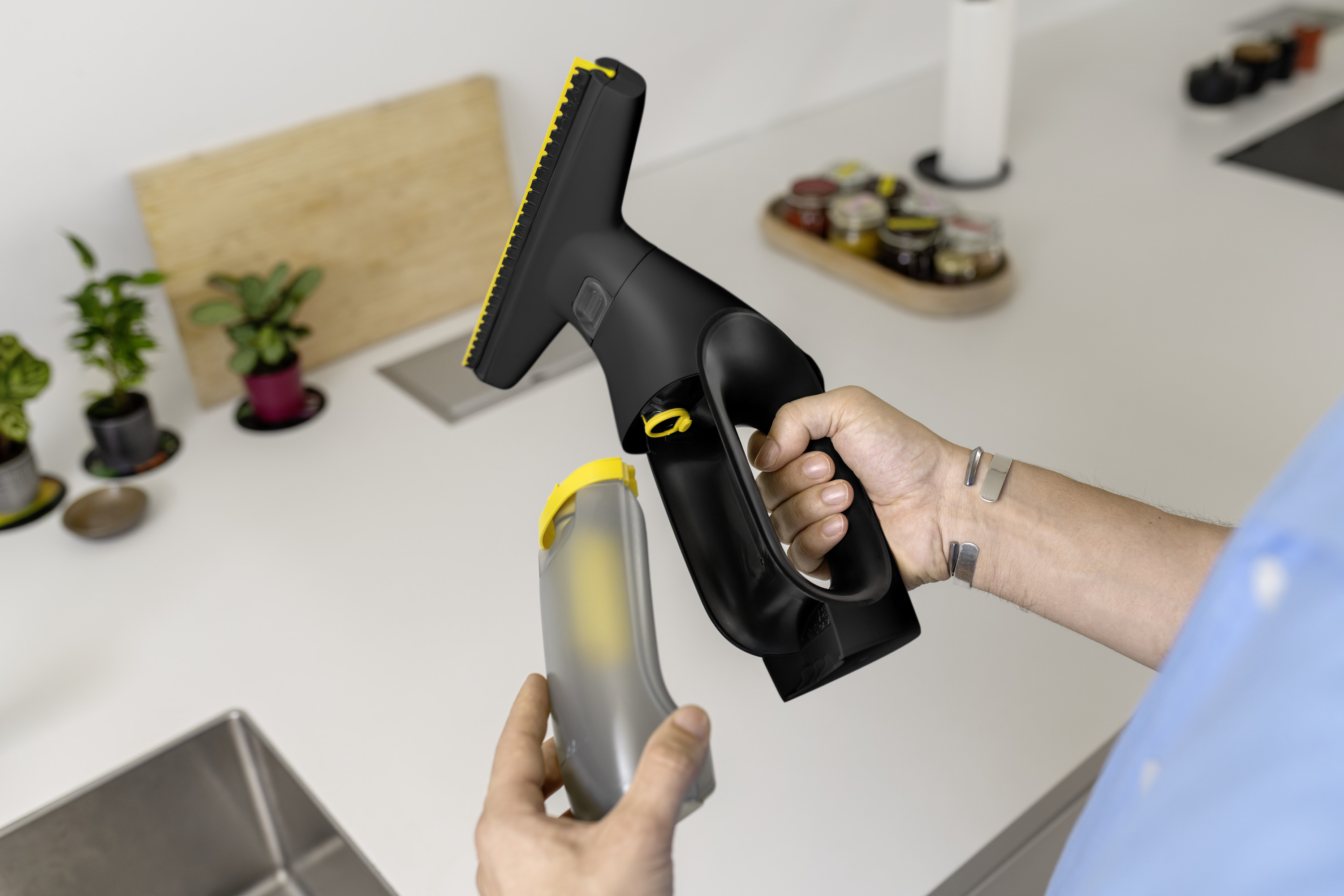Mann hält schwarzen Fensterreiniger mit gelbem Behälter.