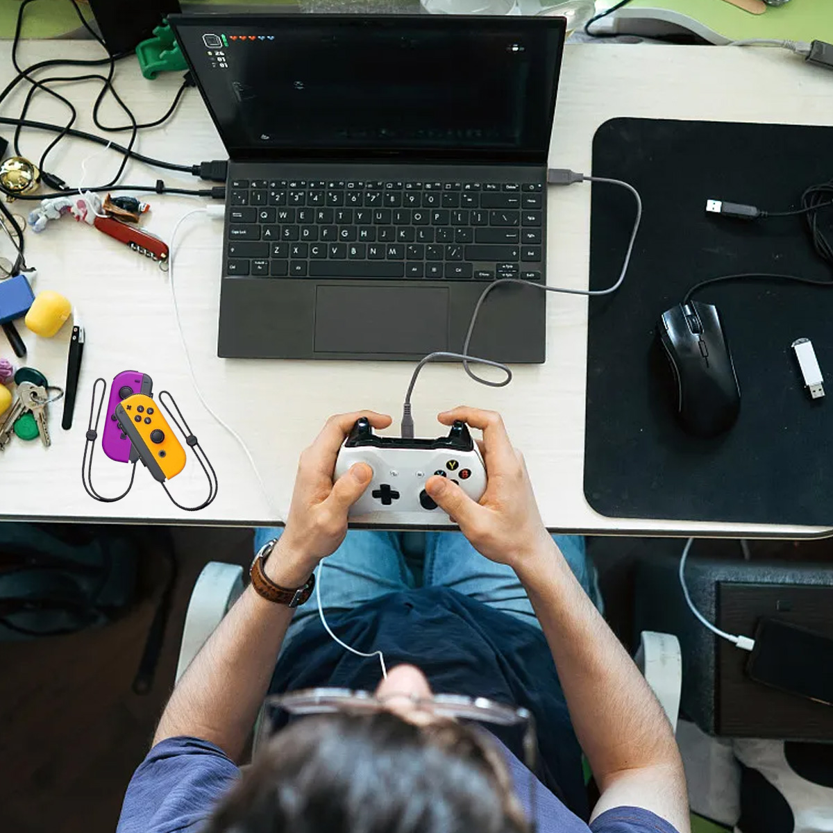 Eine Person spielt Videospiele mit einem Controller, der an einen Laptop angeschlossen ist, Joy-Cons liegen auf dem Schreibtisch.
