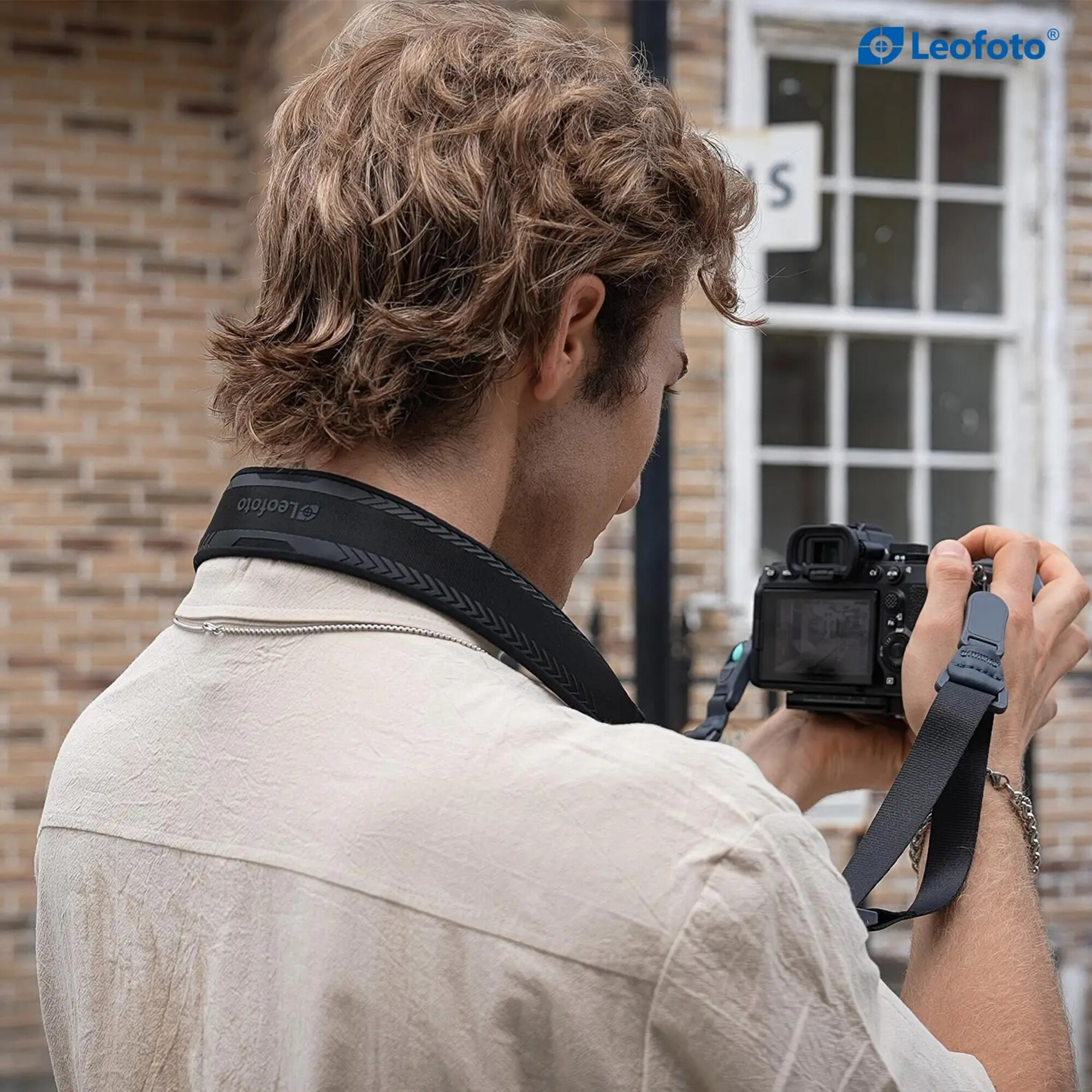 Mann mit lockigem Haar fotografiert mit einer Kamera, trägt ein helles Hemd.