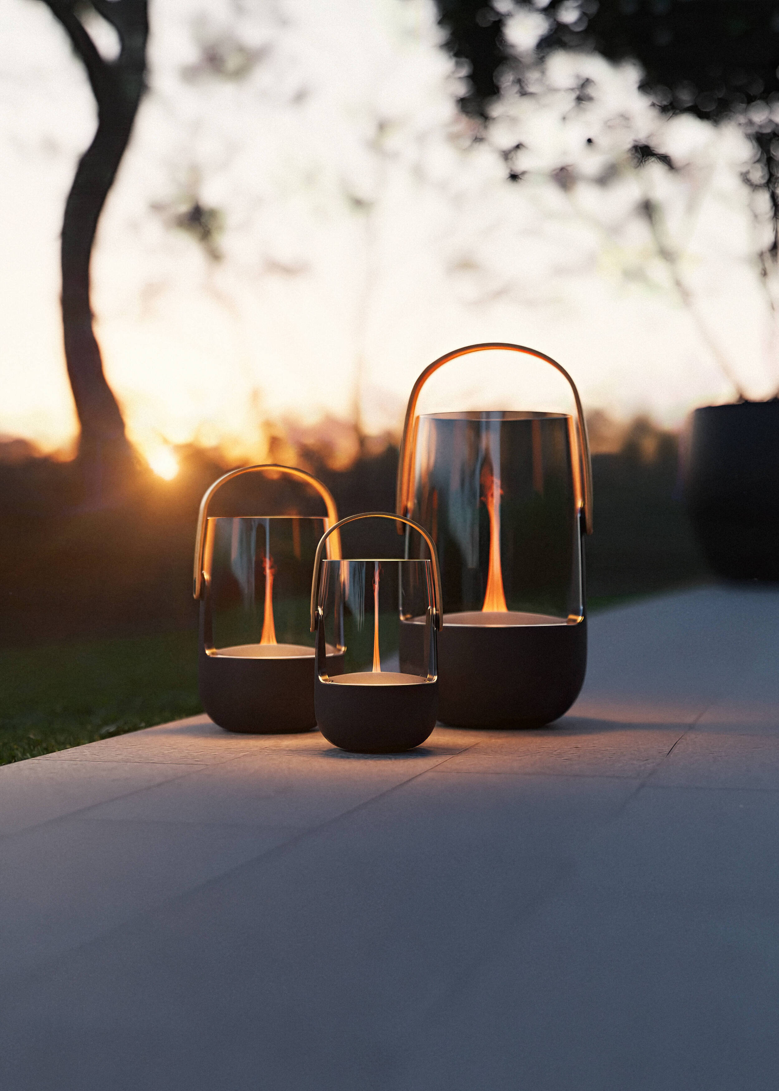 Three lanterns with flame lights stand outdoors at sunset.