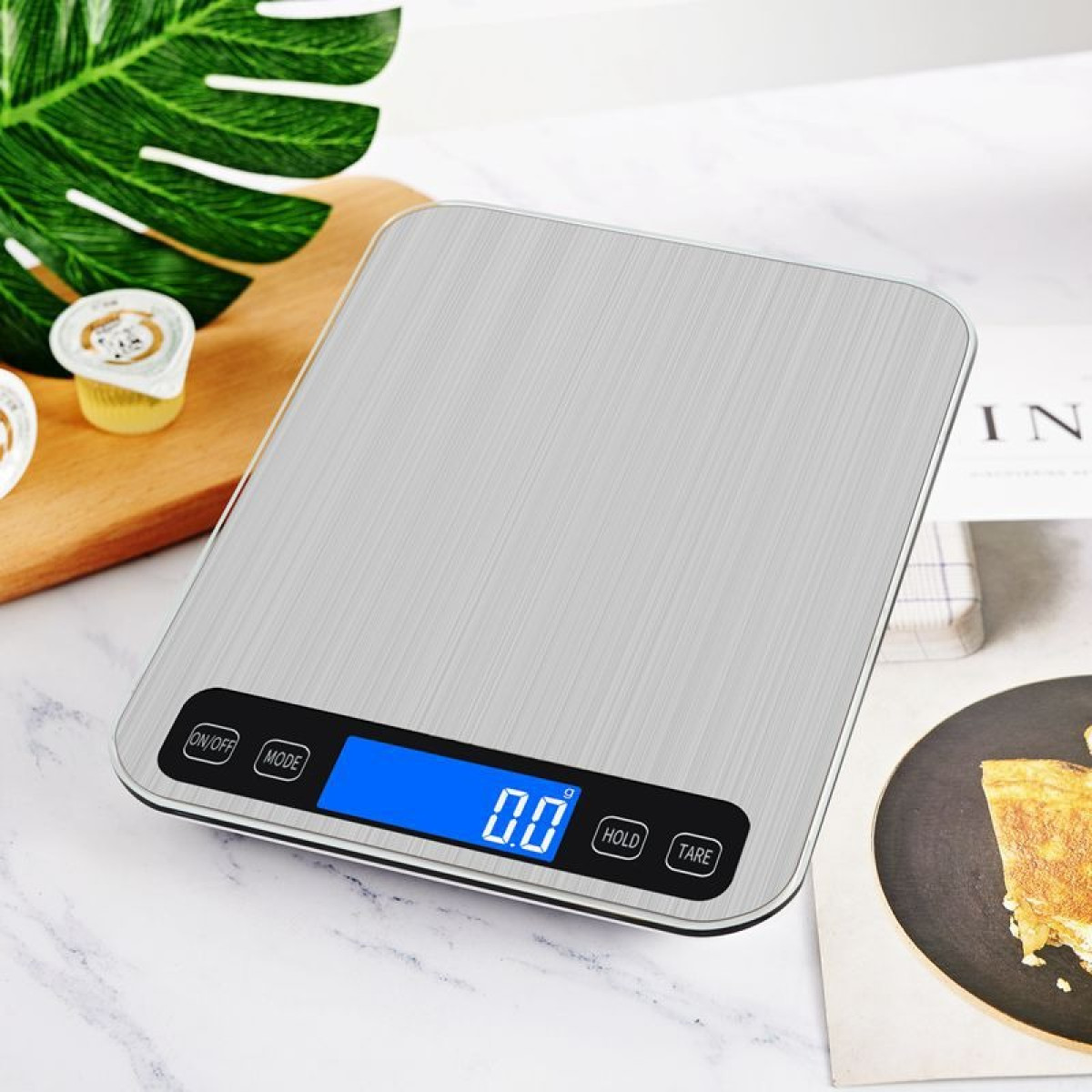Eine digitale Küchenwaage aus gebürstetem Metall mit blauem LCD-Display steht auf einer Marmoroberfläche.