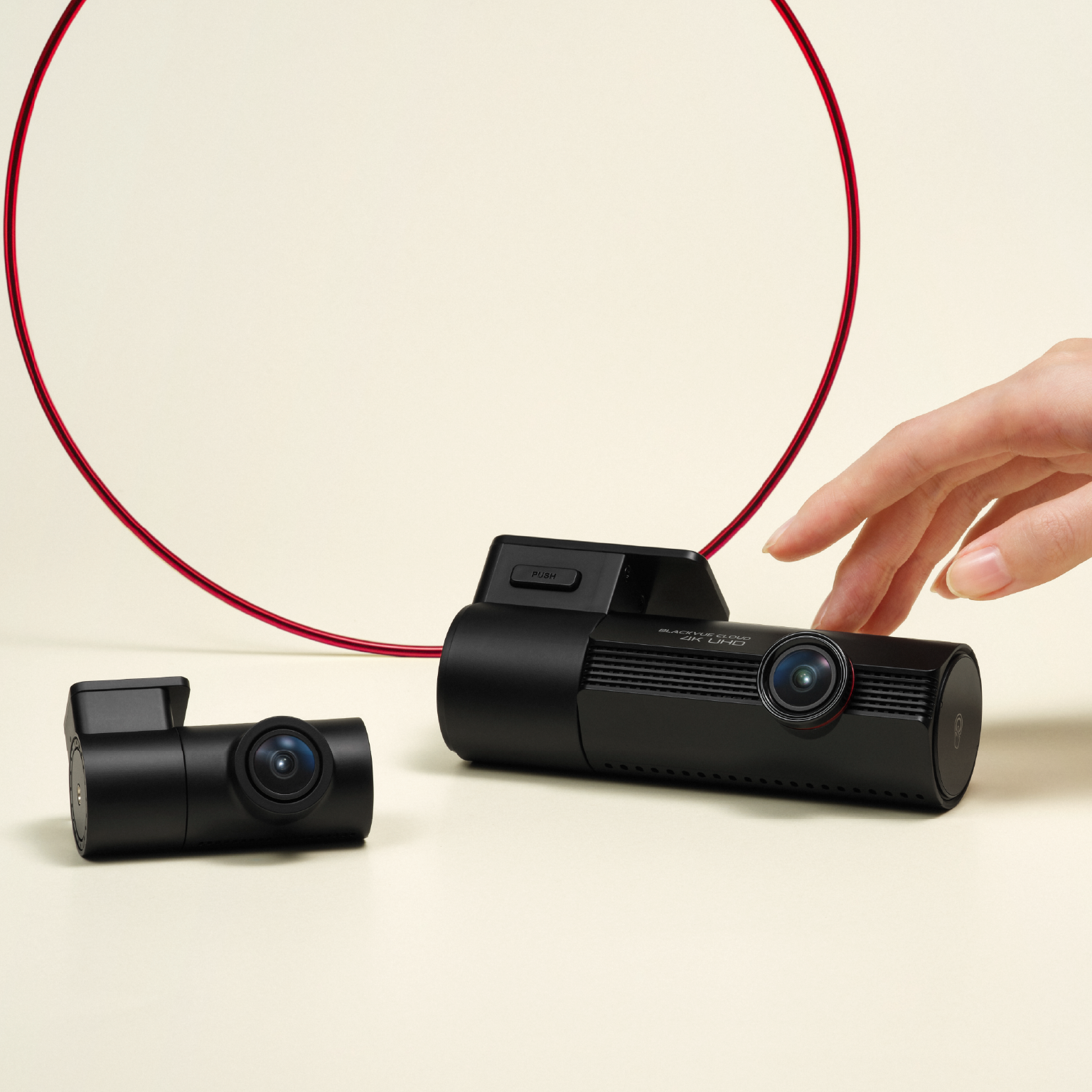 Twee zwarte dashcams op lichte ondergrond, met rode ring en hand nabij.