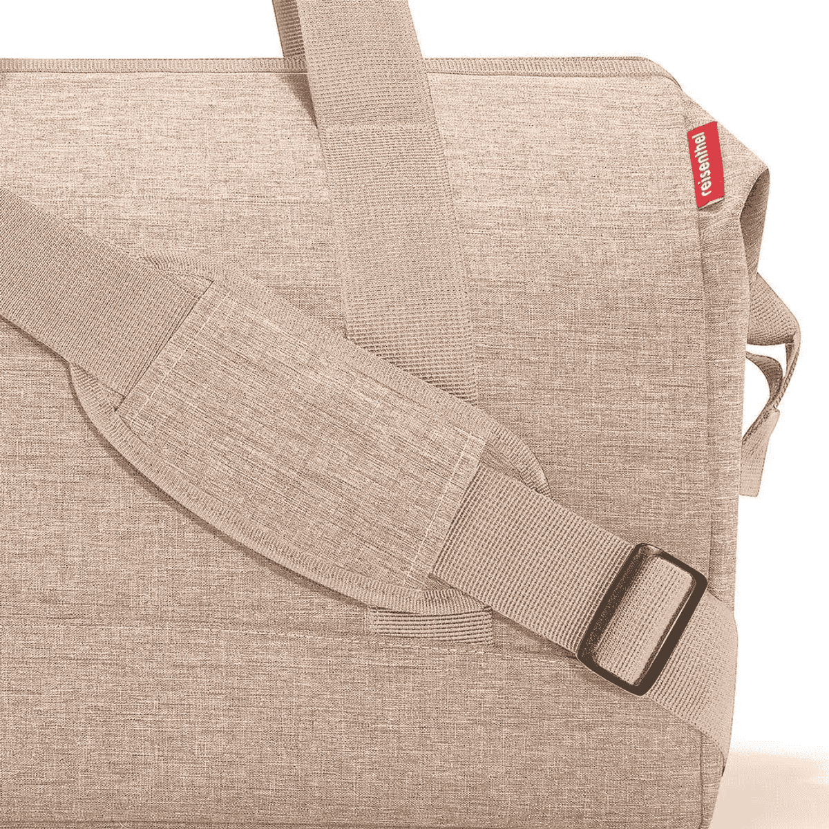 Primer plano de bolsa de lona beige con correa ajustable y etiqueta roja.