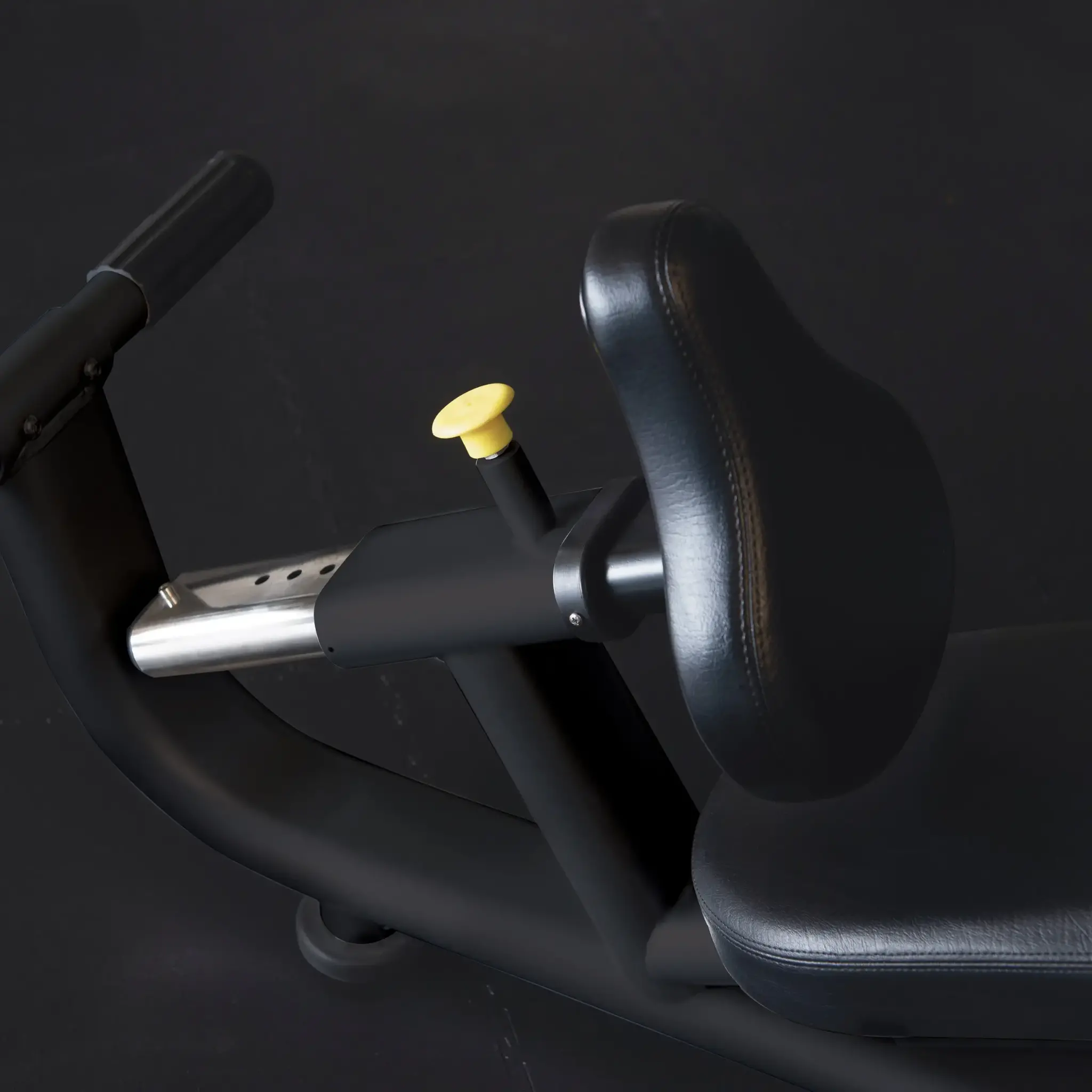 Black exercise bike seat with yellow adjustment knob and silver handle.