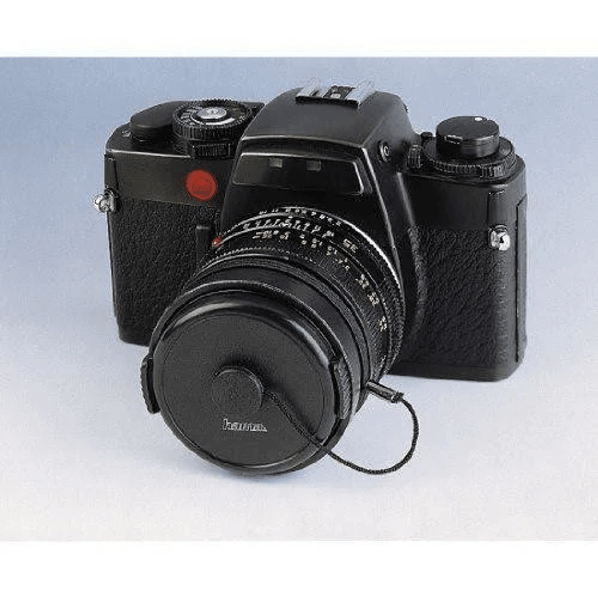 Una fotocamera nera con obiettivo e tappo su sfondo chiaro.