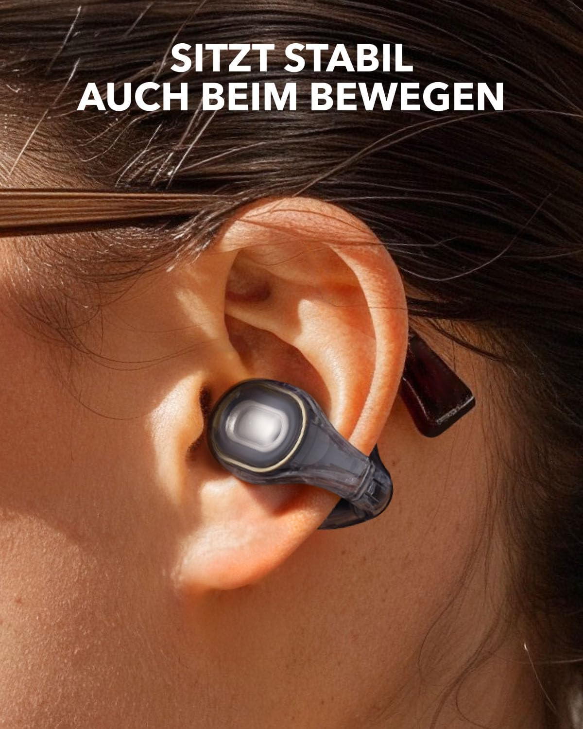 Ein schwarzer Kopfhörer sitzt im Ohr einer Person, umgeben von dunklem Haar.