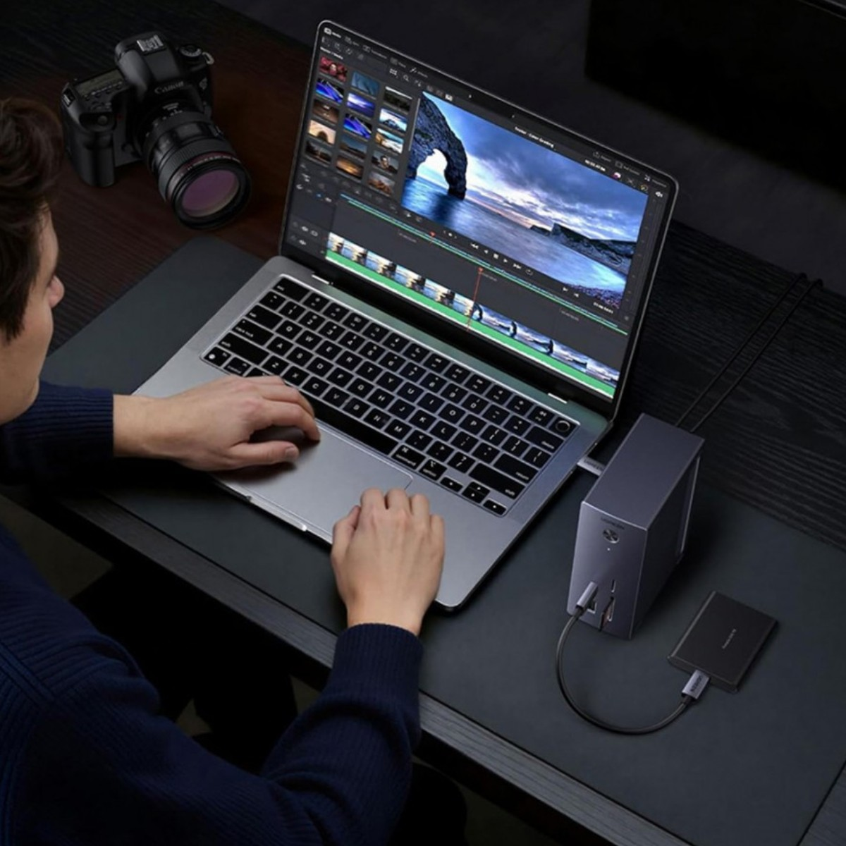 Un uomo edita video su un laptop accanto a una fotocamera e un dock.