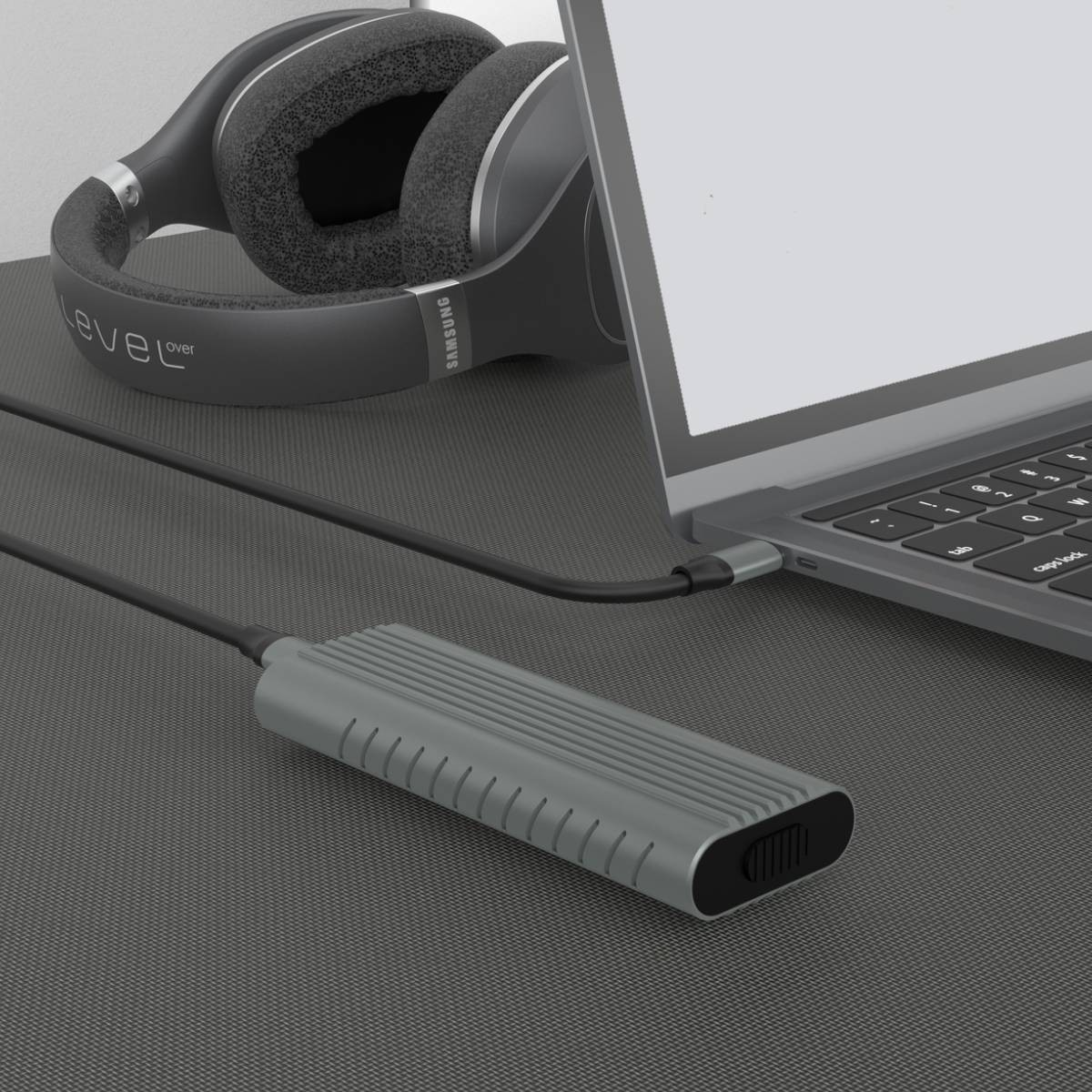 Un disco duro externo gris se conecta a un portátil, con auriculares cerca.