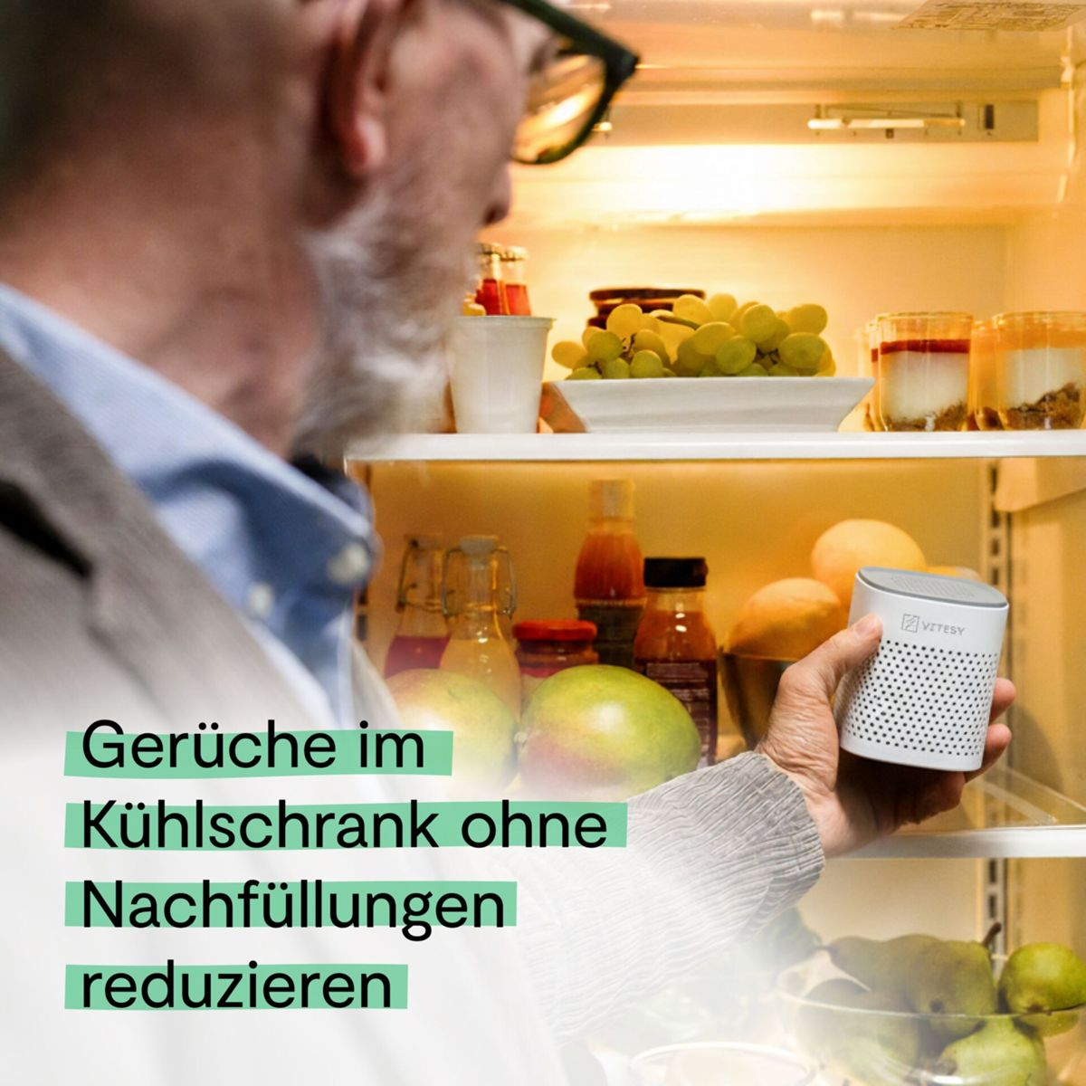 Mann hält ein kleines weißes Gerät im Kühlschrank voller Obst und Getränke.