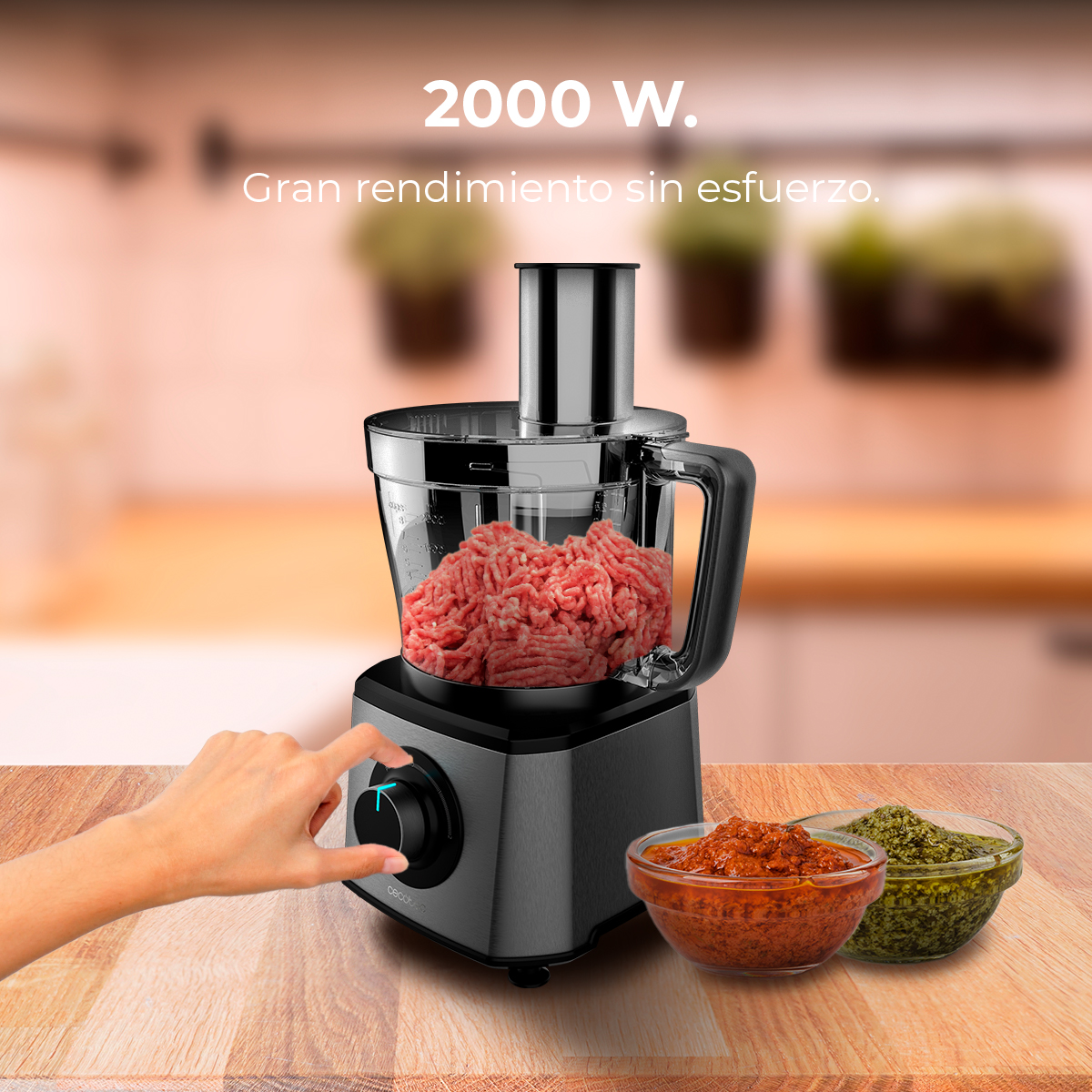 Un procesador de alimentos con carne picada cruda, dos cuencos de salsa y una mano girando un botón.