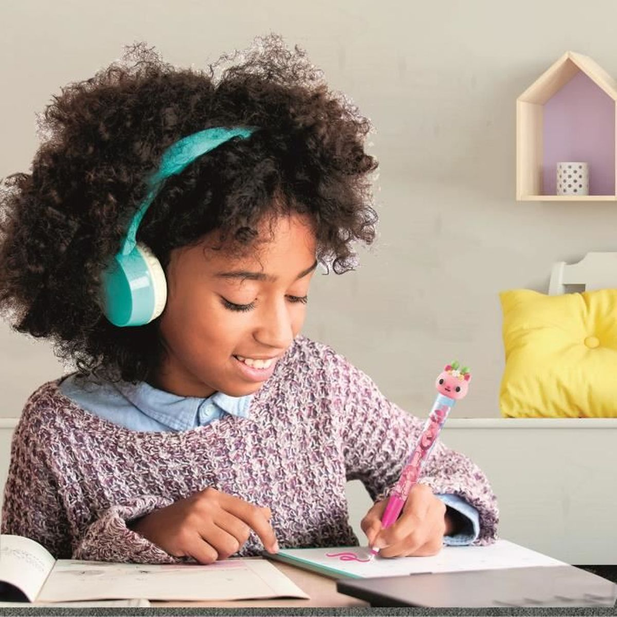 Una bambina con le cuffie scrive con una penna colorata. Cuscino giallo sullo sfondo.
