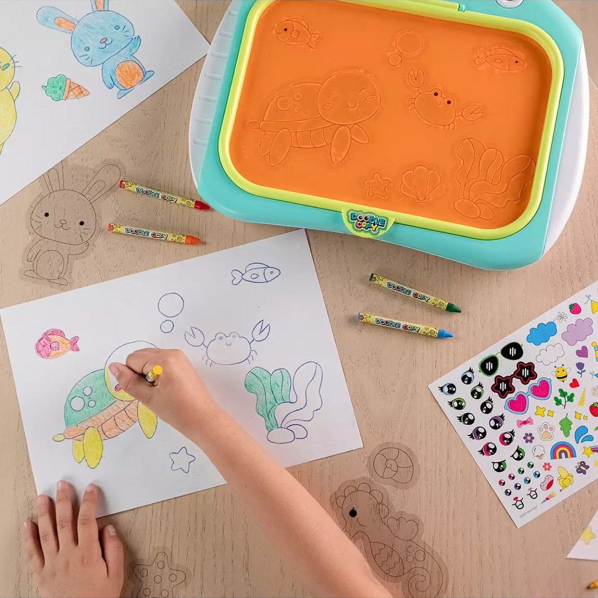 Un bambino colora una tartaruga su carta con pastelli accanto a una lavagna da disegno e adesivi.