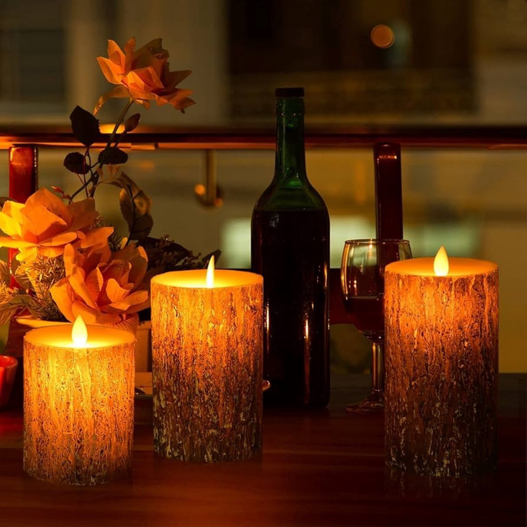 Three flickering LED candles with wood texture, a wine bottle, and flowers on a table.