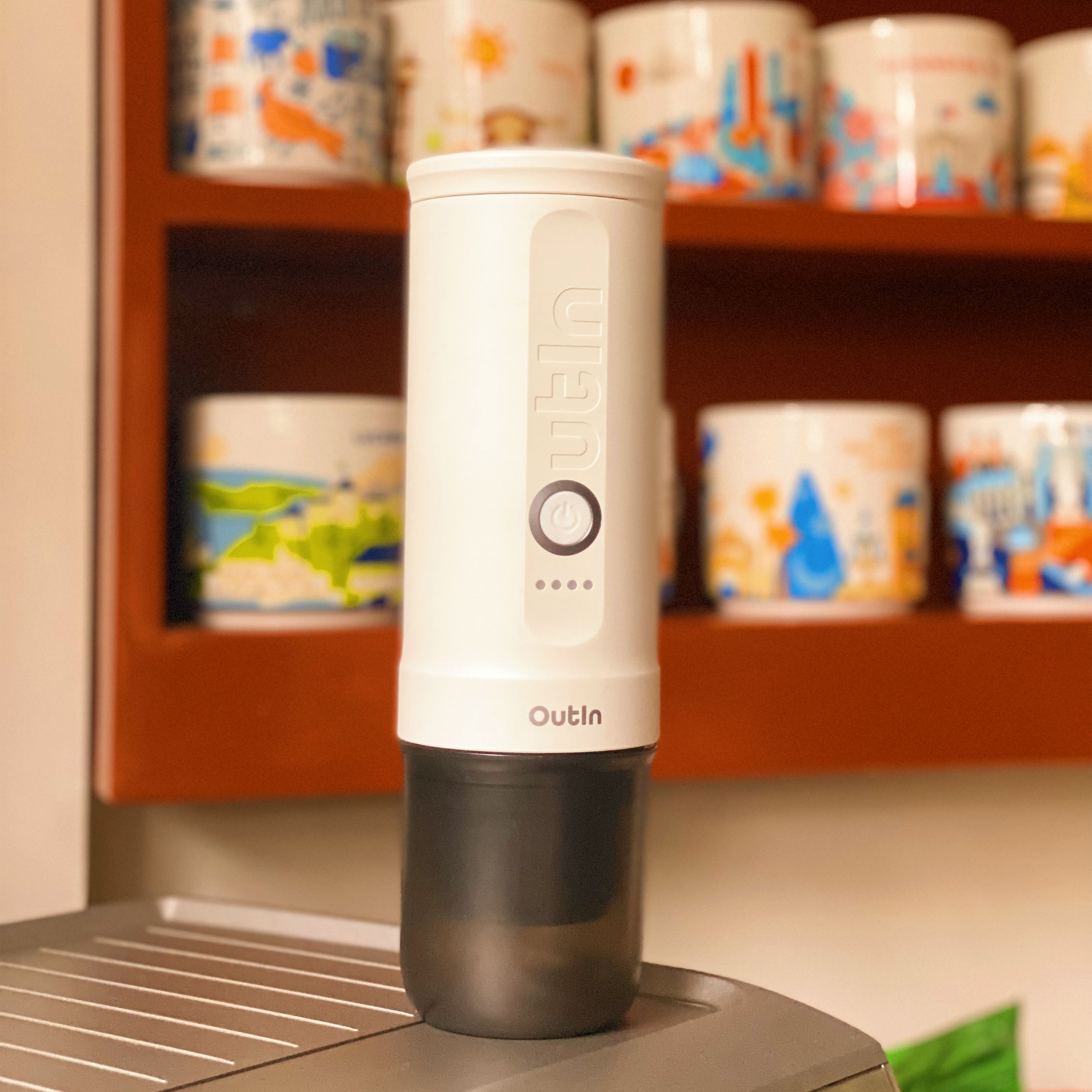 Un recipiente blanco con logo "Outin" descansa sobre una rejilla. Tazas en el estante.