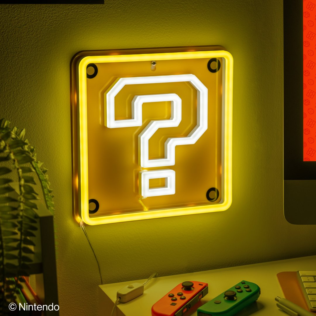 Żółta neonowa lampa z znakiem zapytania na ścianie nad dwoma kontrolerami.