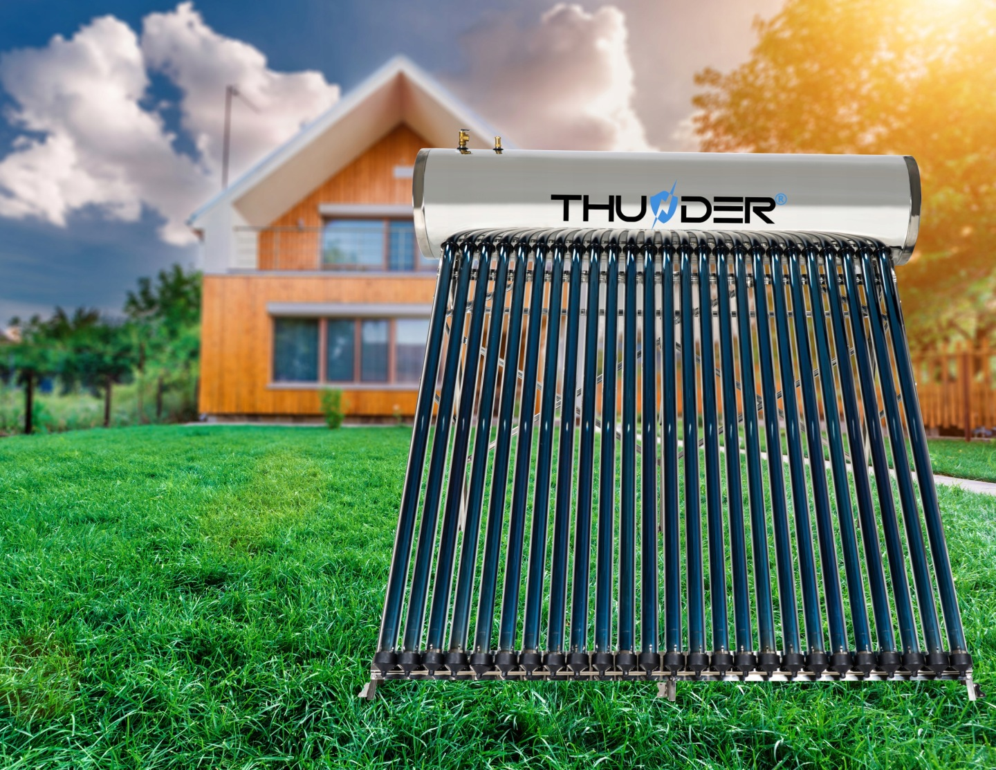 Kolektor solarny z niebieskimi rurami stoi na zielonej trawie przed drewnianym domem.