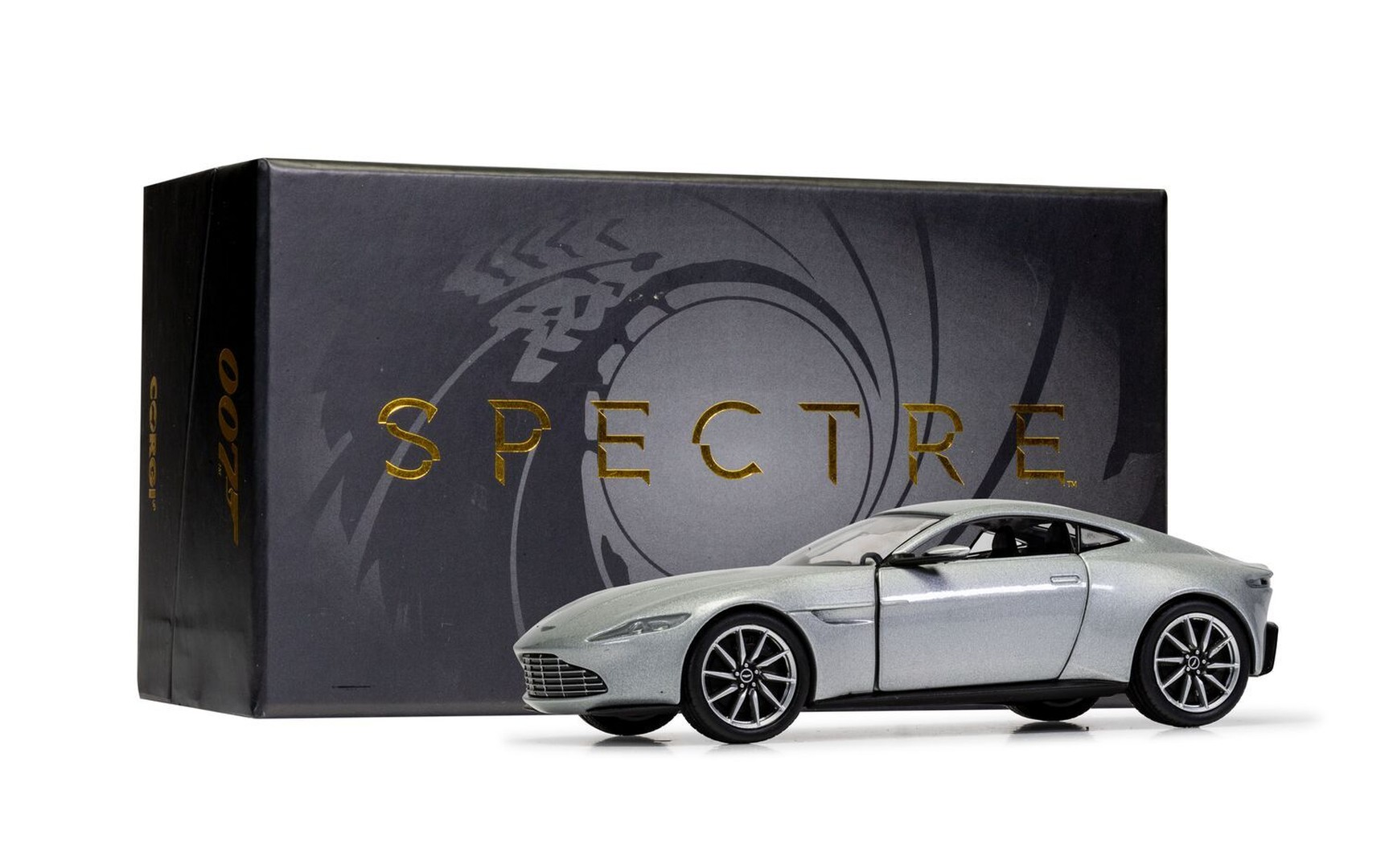 Srebrny Aston Martin DB10 obok czarnego pudełka "Spectre" z logo 007.