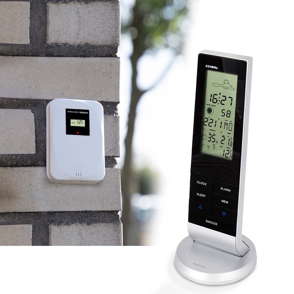 Weißer Funksensor an Ziegelwand, neben digitaler Wetterstation mit Uhrzeit und Temperatur.