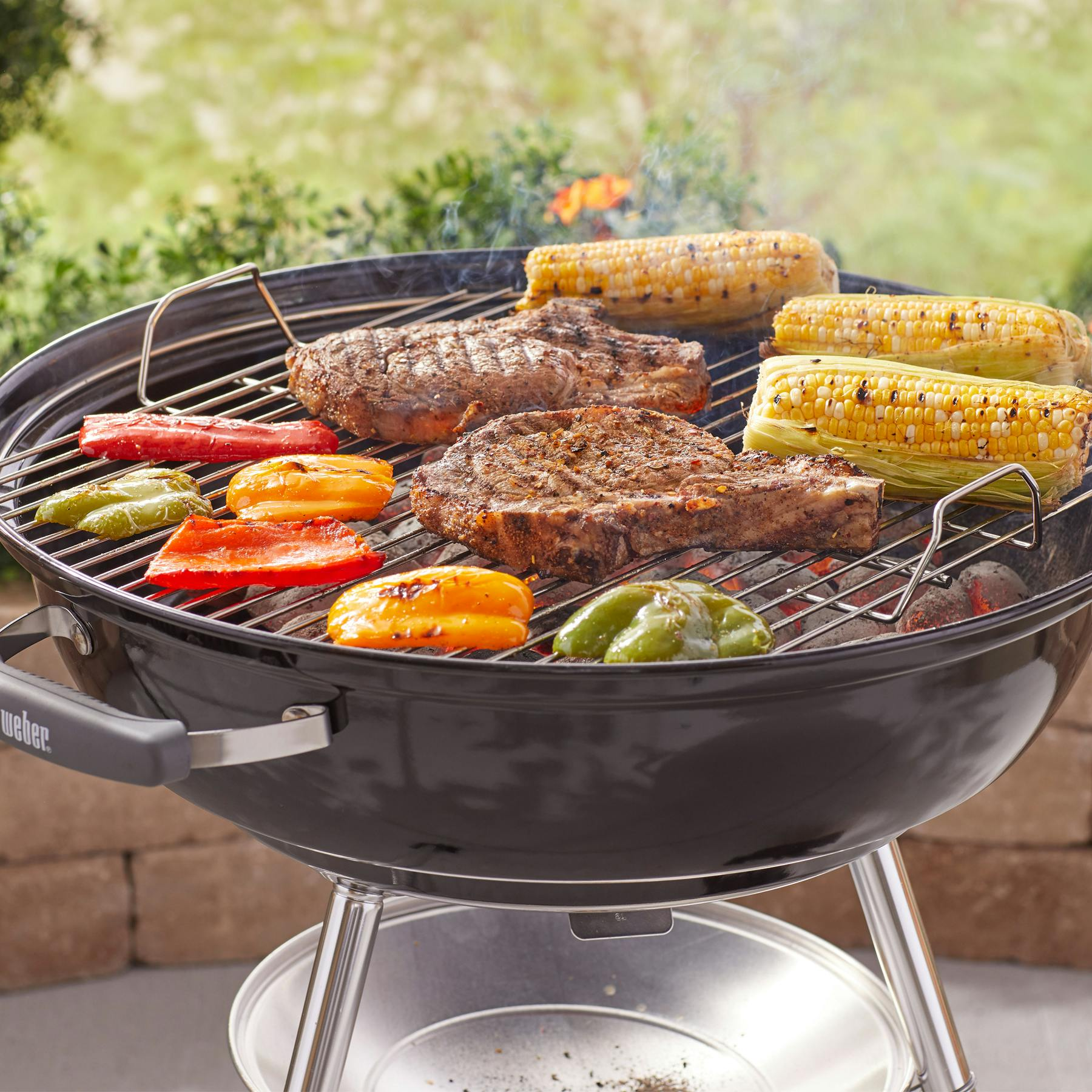 Steaks und Maiskolben garen auf einem Holzkohlegrill mit Paprikastücken.