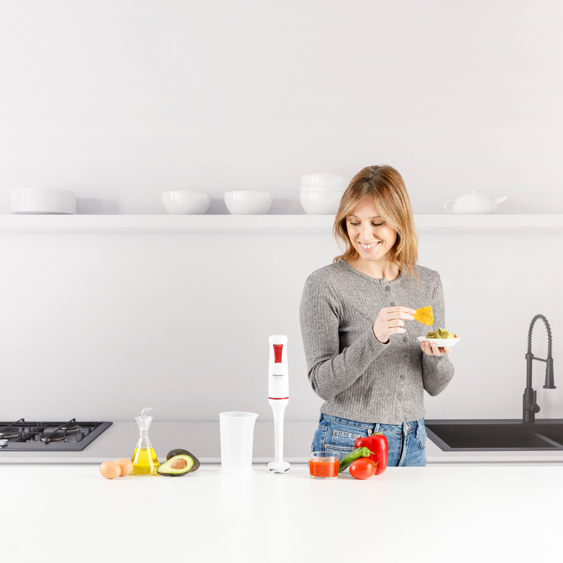 Eine Frau isst Guacamole mit einem Chip in einer modernen Küche.