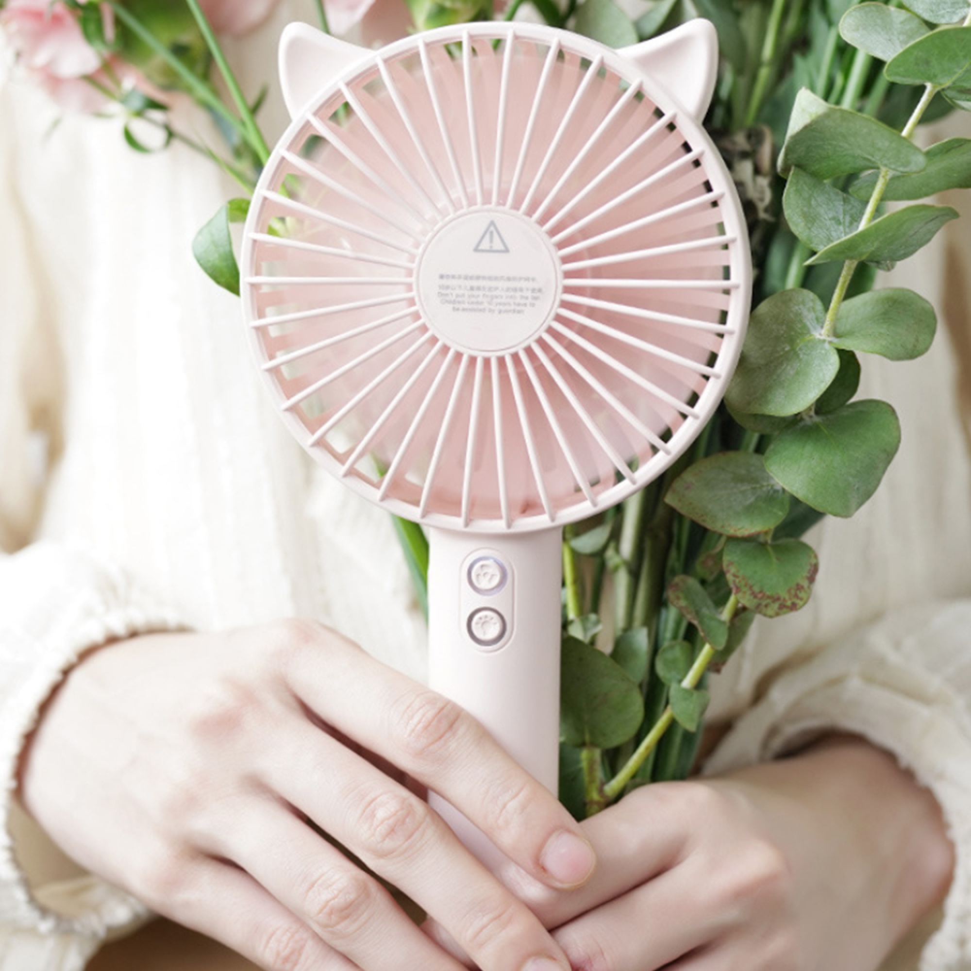 Eine Person hält einen rosafarbenen Ventilator mit Katzenohren und Blumen.
