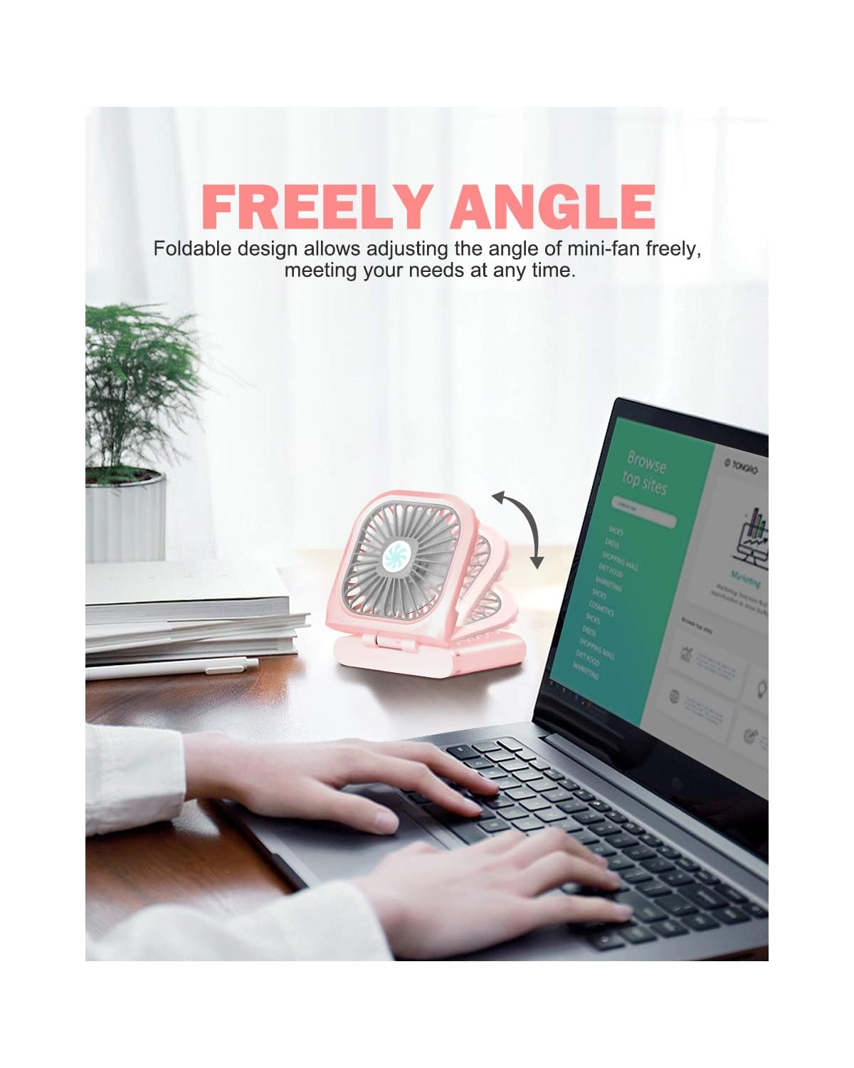 Eine rosa Mini-Ventilator steht auf einem Schreibtisch neben einem Laptop, auf dem eine Person tippt.