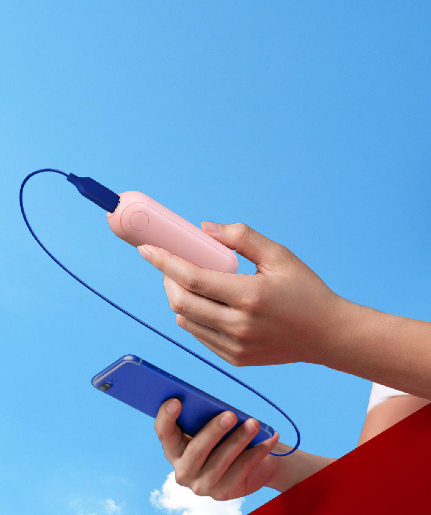 Eine Person lädt ein blaues Handy mit einer pinken Powerbank vor blauem Himmel.