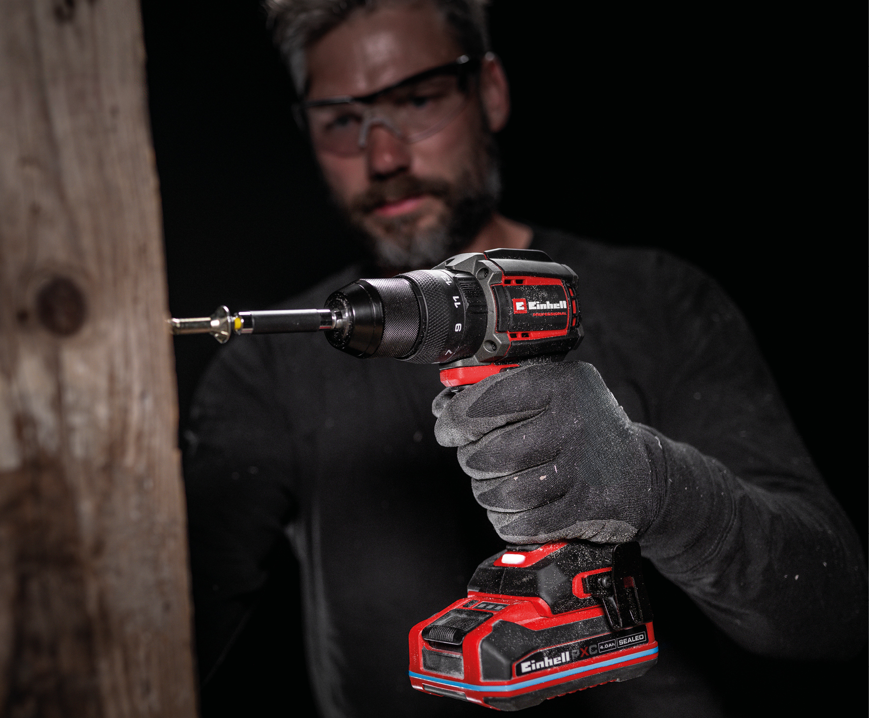 Mann mit Schutzbrille bohrt mit Akkuschrauber in Holz. Nahaufnahme.