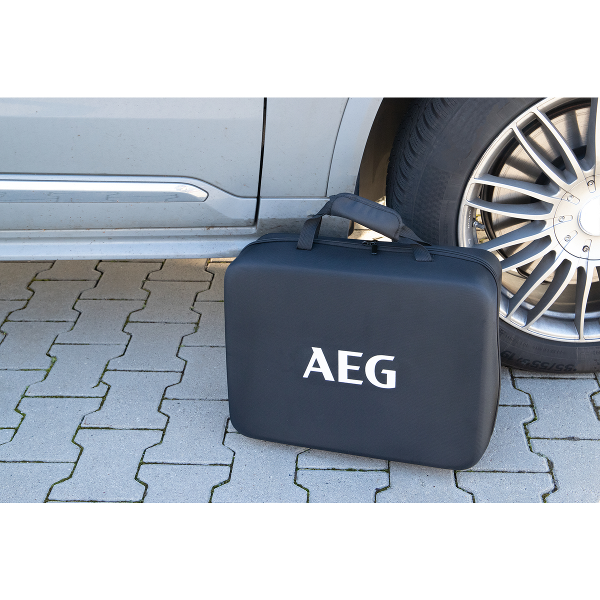 Schwarze AEG-Tasche neben einem Auto auf einem gepflasterten Weg.