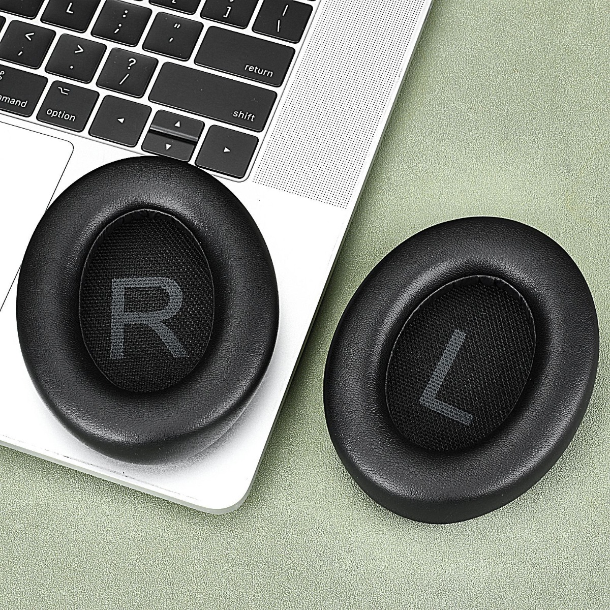 Zwei schwarze Kopfhörer-Ohrpolster, eines mit R, das andere mit L, auf einer Laptop-Tastatur.