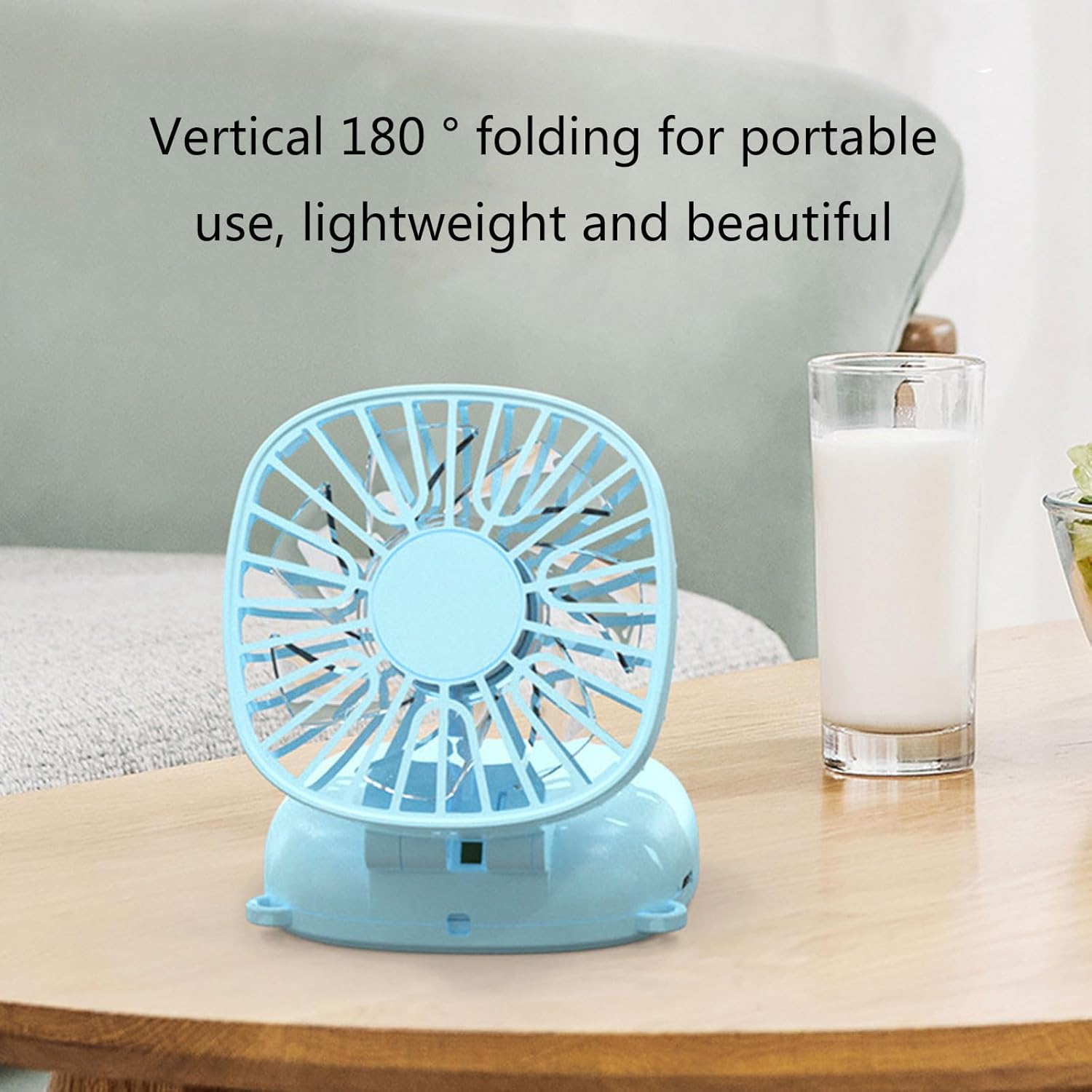 Ein kleiner blauer Ventilator steht auf einem Holztisch neben einem Glas Milch.