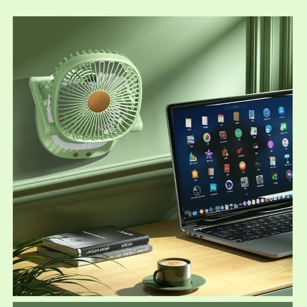 Ein grüner Schreibtischventilator ist an einer hellgrünen Wand montiert. Laptop, Bücher und Kaffeetasse auf dem Schreibtisch.