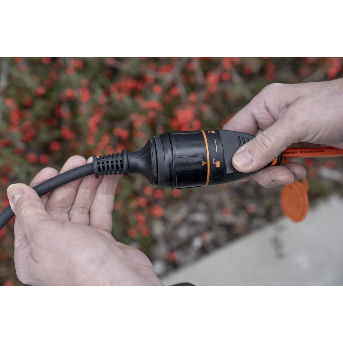 Hände verbinden ein schwarzes Stromkabel mit einem schwarzen und orangen Stecker.