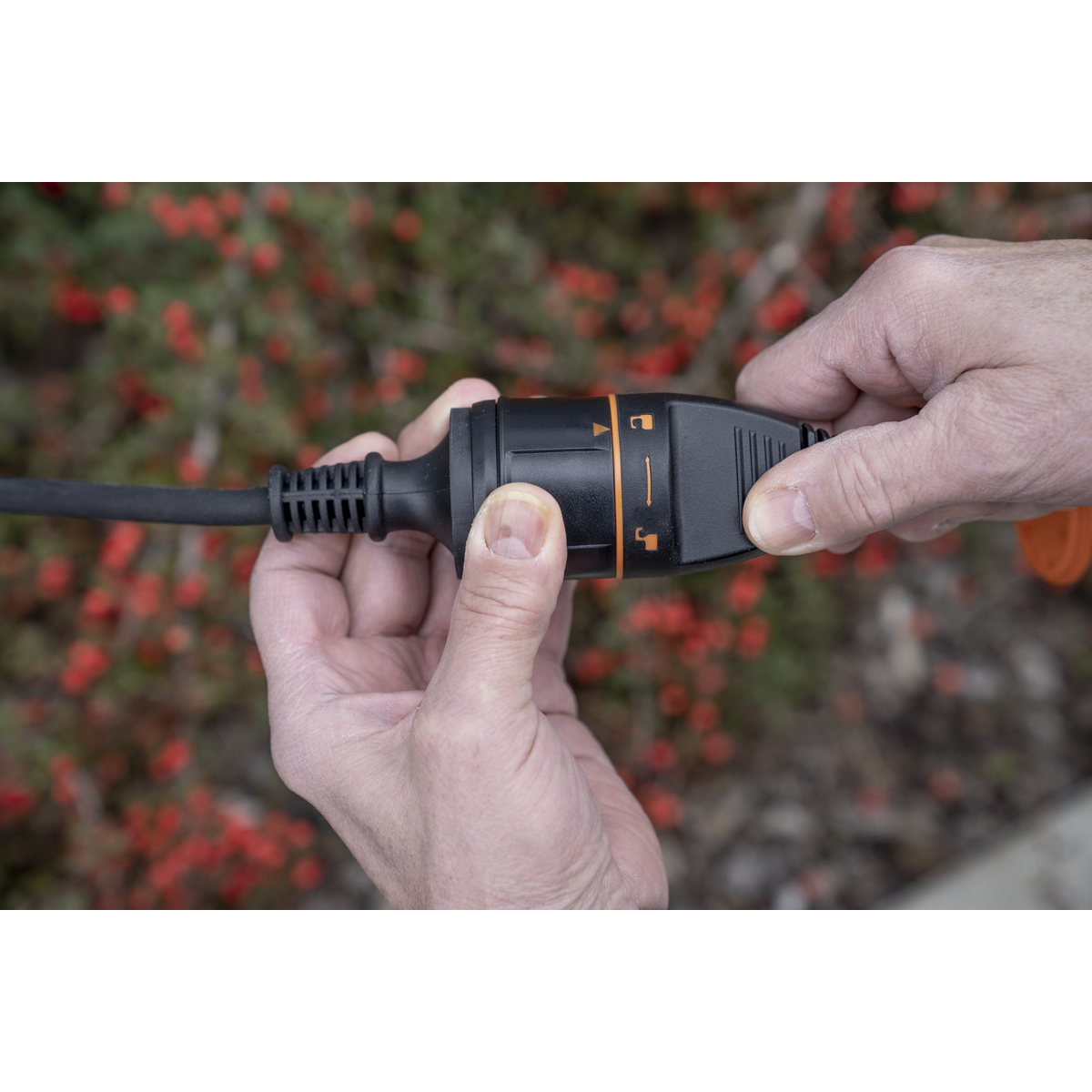 Hände verbinden einen schwarzen Stecker mit orangen Markierungen mit einem Verlängerungskabel.