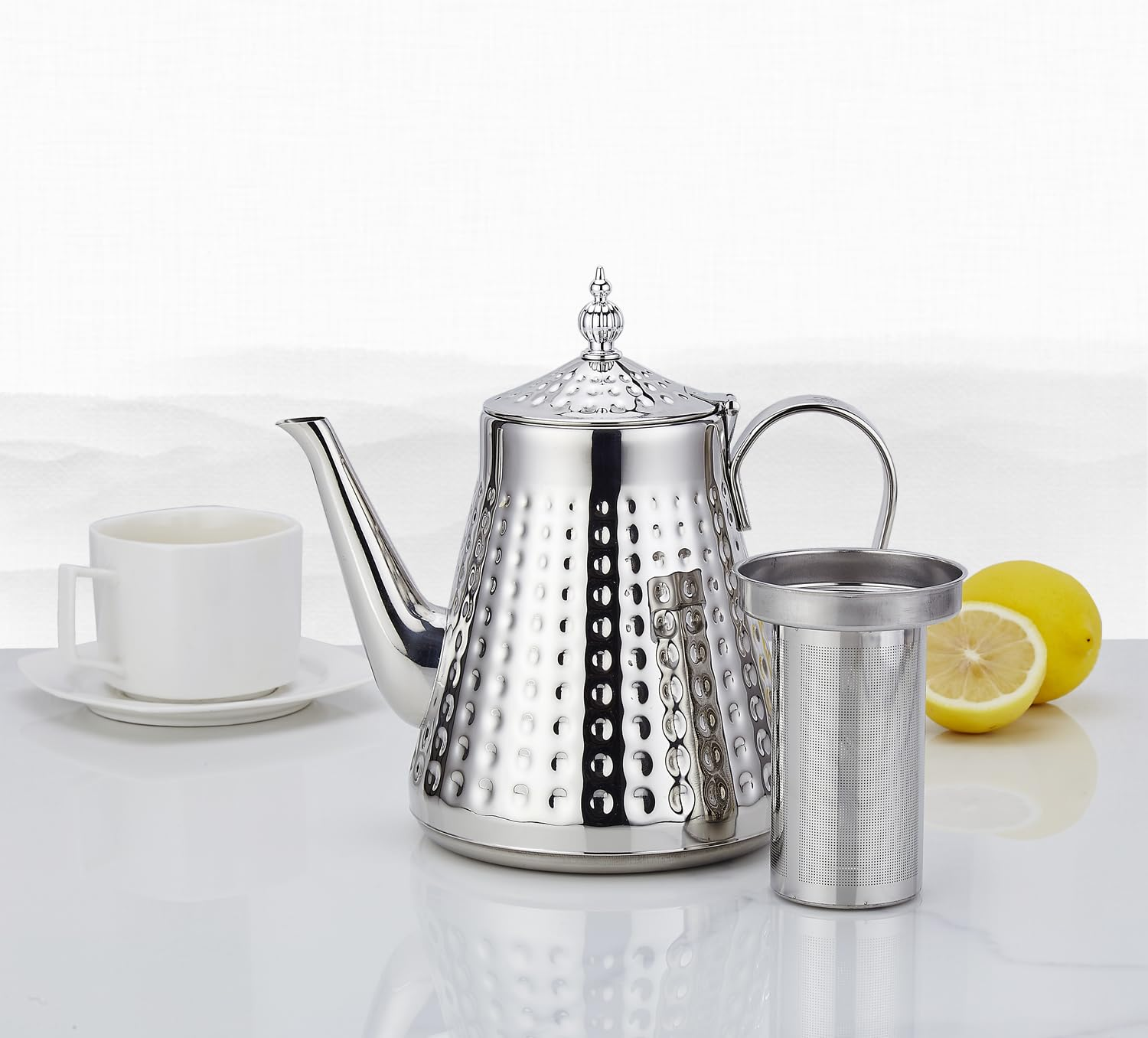 Silberne Teekanne mit Becher, Sieb und Zitronen.