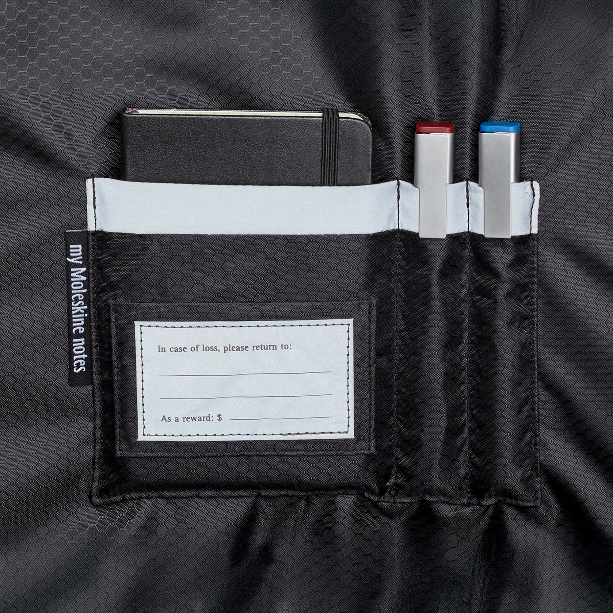 Tasca nera con taccuino e due penne. Etichetta: 'my Moleskine notes'.