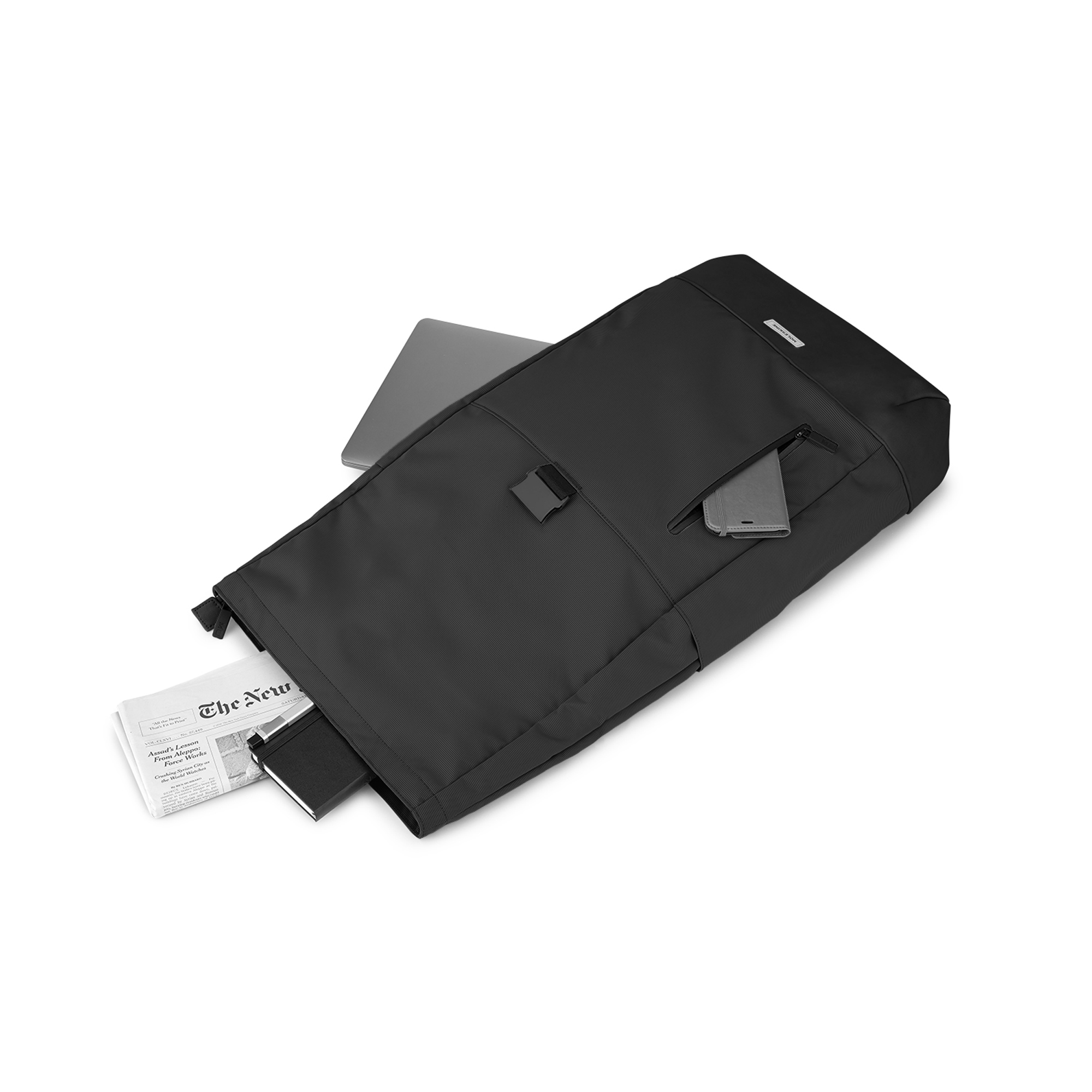 Zaino nero con laptop, telefono e giornale. Un taccuino sporge.