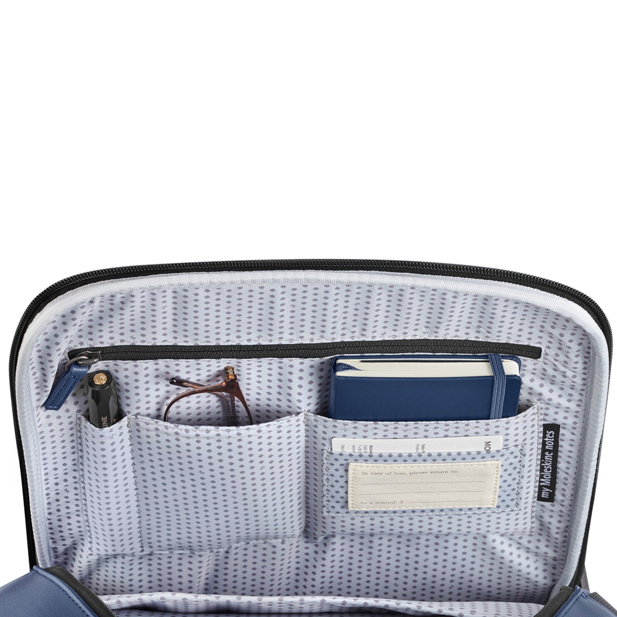 Interno borsa aperta con penna, occhiali, taccuino blu ed etichetta di reso.